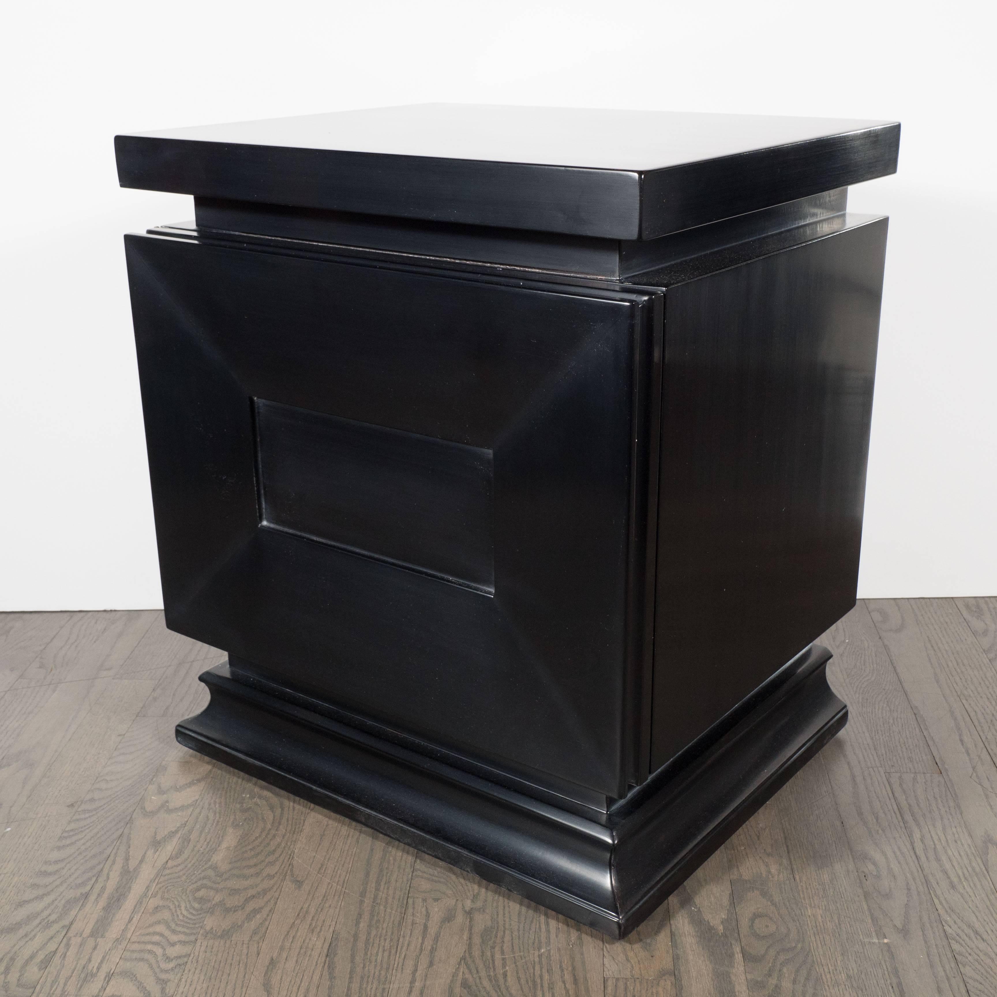 A pair of Mid-Century modernist nightstands or end tables in hand-rubbed ebonized walnut, featuring a shadowbox design. Stepped bases support shadowbox segmented doors which are supported by brass hinges, which each door opening outward to reveal a