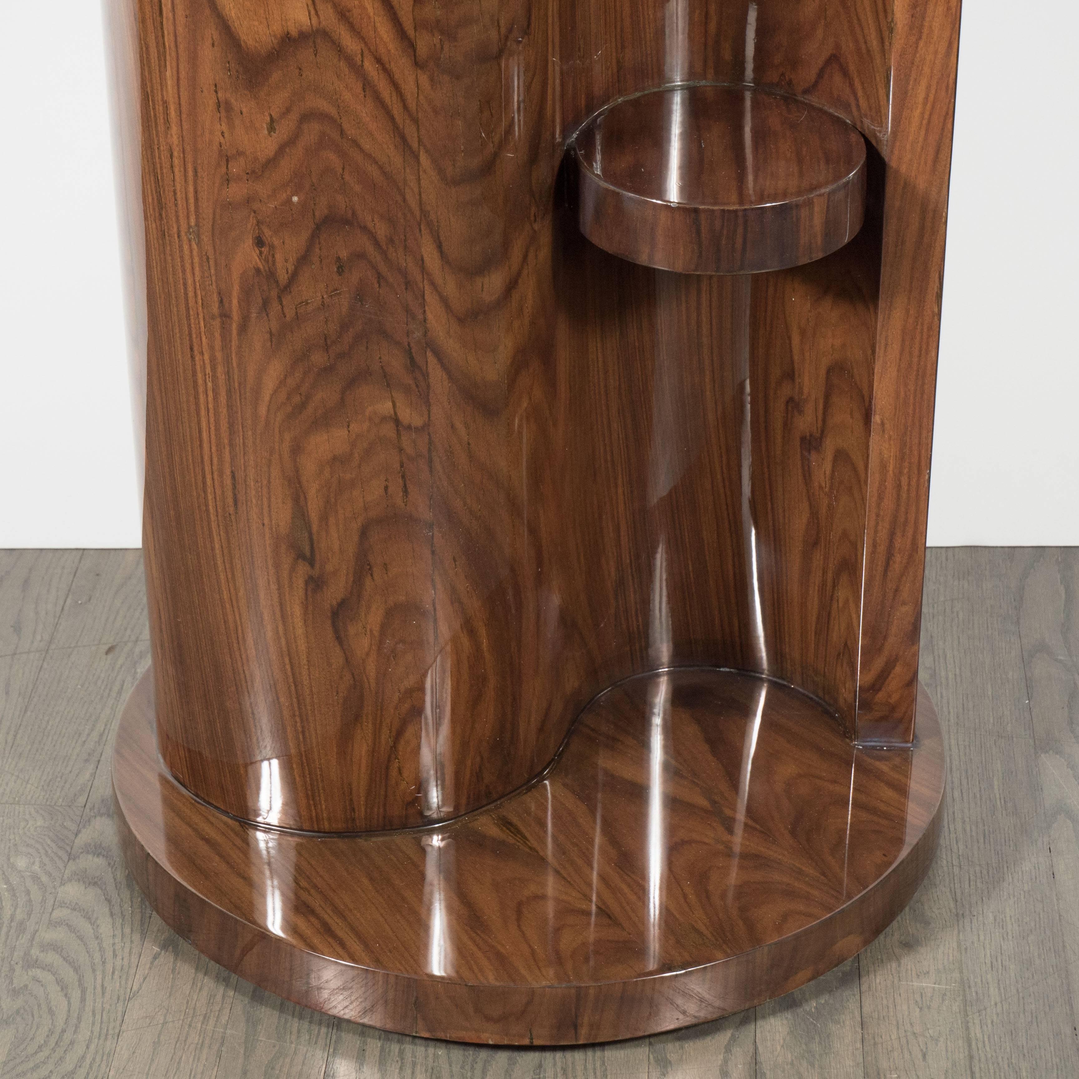 This stunning Art Deco occasional table/ pedestal in bookmatched burled walnut was realized in France circa 1935. It features a circular walnut base that supports an S-form body composed of two seamlessly adjoined streamlined forms, each with a