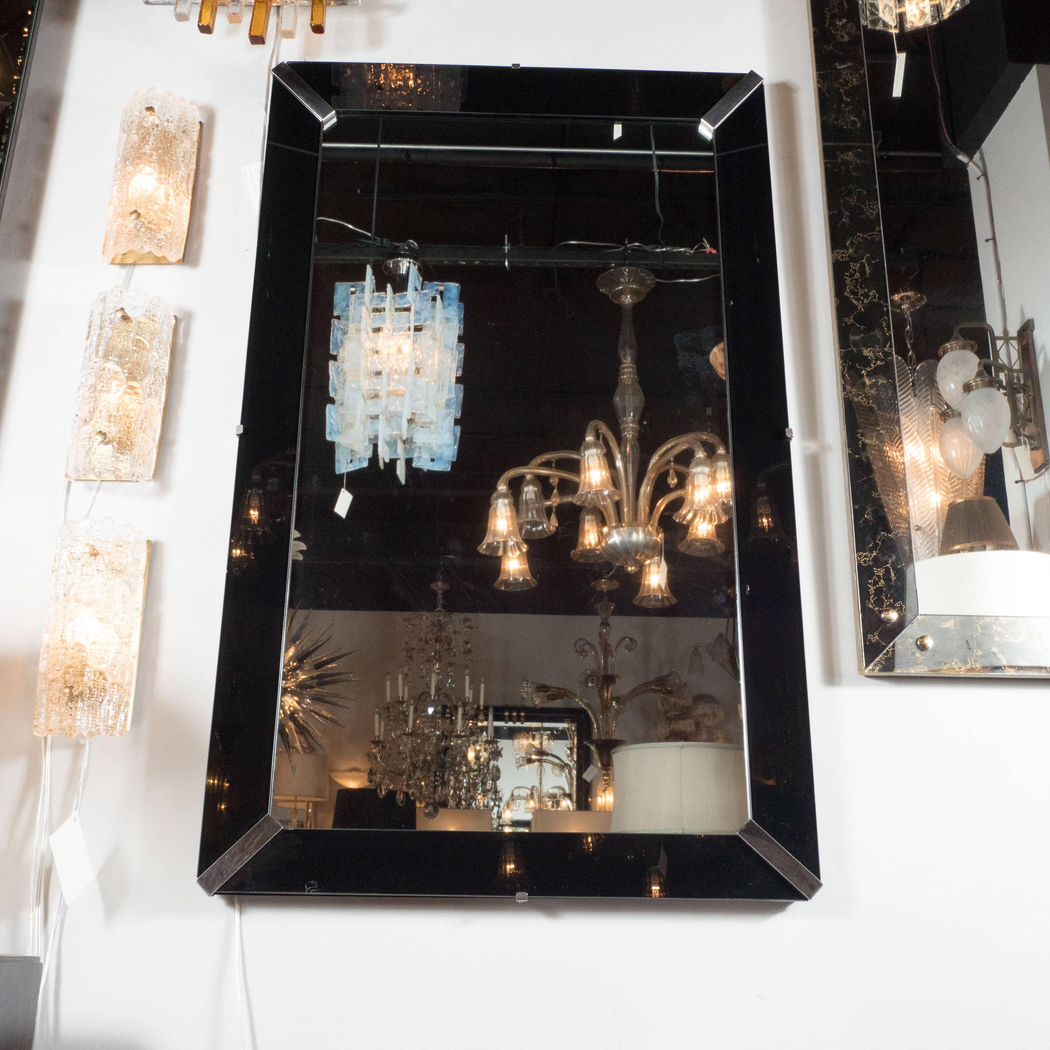 An Art Deco skyscraper style paneled mirror with a vitrolite black glass segmented border. Chrome details adorn the corners of this piece and connect the outer glass frame. This piece can be hung wither horizontally or vertically. It is in excellent