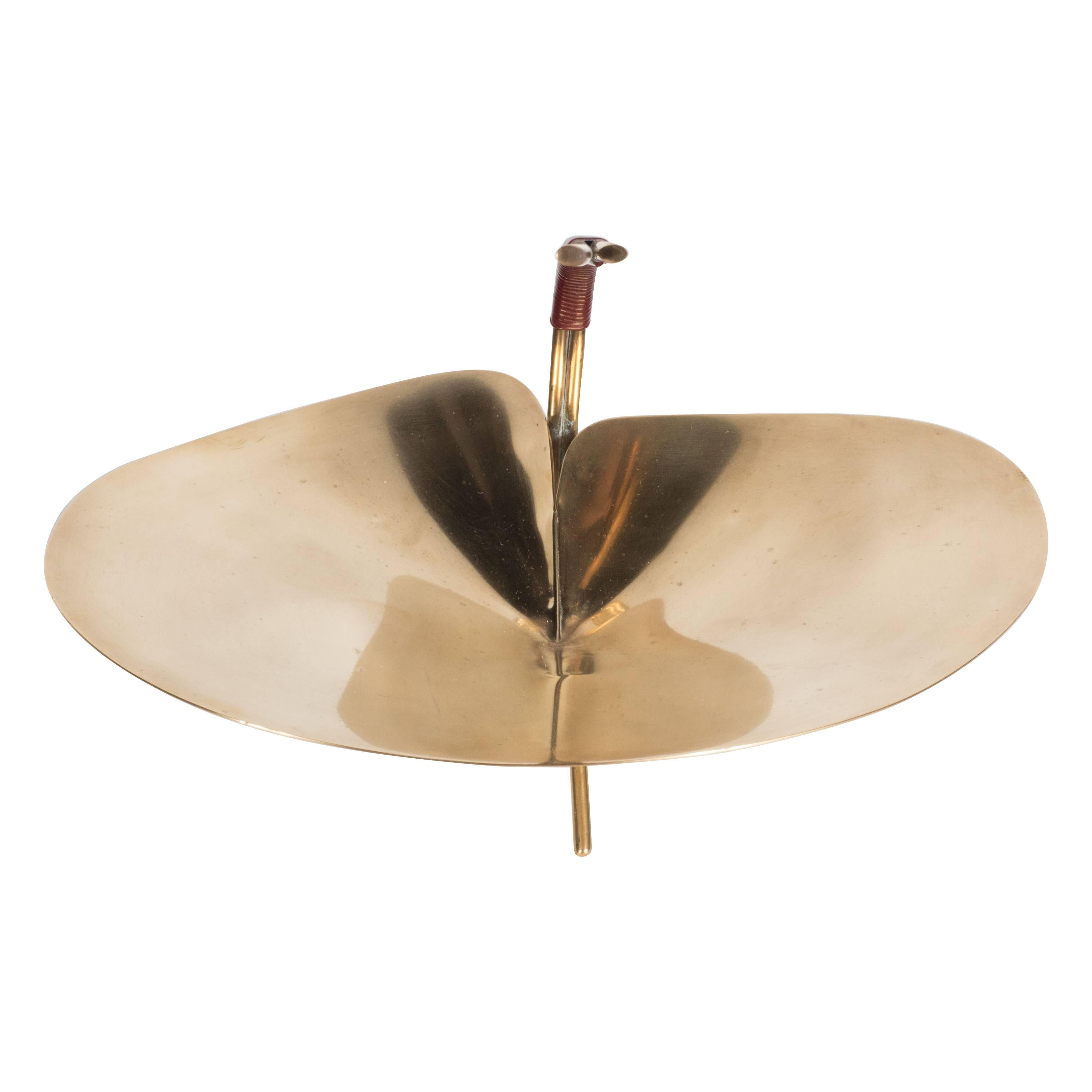 A Mid-Century Modern polished brass lilypad dish by Carl Auböck. Three pronged tubular brass feet support a single sheet of polished brass in the form of a lilypad. A double-stem wrapped in tightened rattan banding merges them together. This piece
