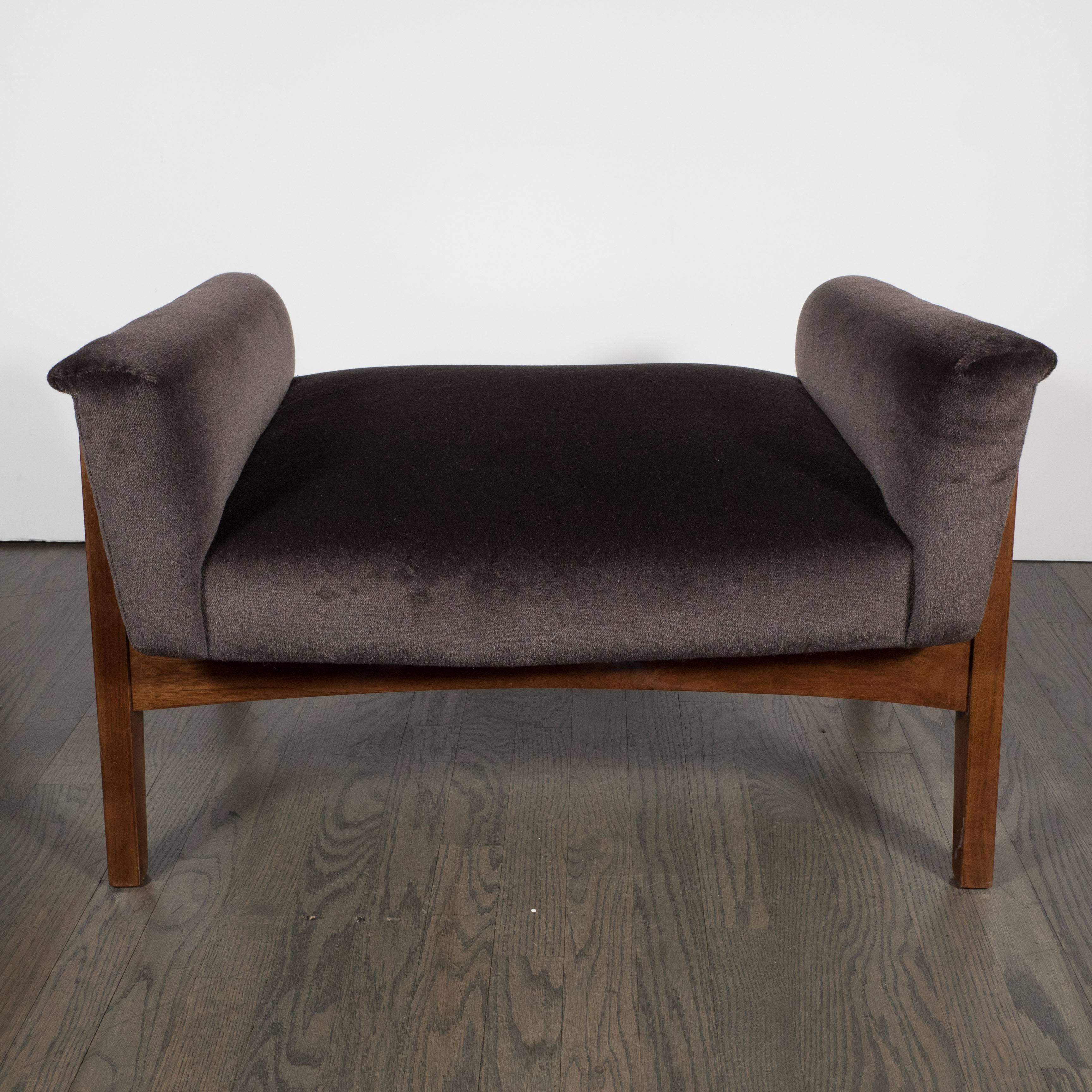 A Mid-Century Modernist footstool in chocolate mohair and hand-rubbed walnut base. A slanted, U-shaped upholstered seat rests on a splayed base in hand-rubbed walnut. A lovely piece of 1950s American Mid-Century design and quality. It has been mint