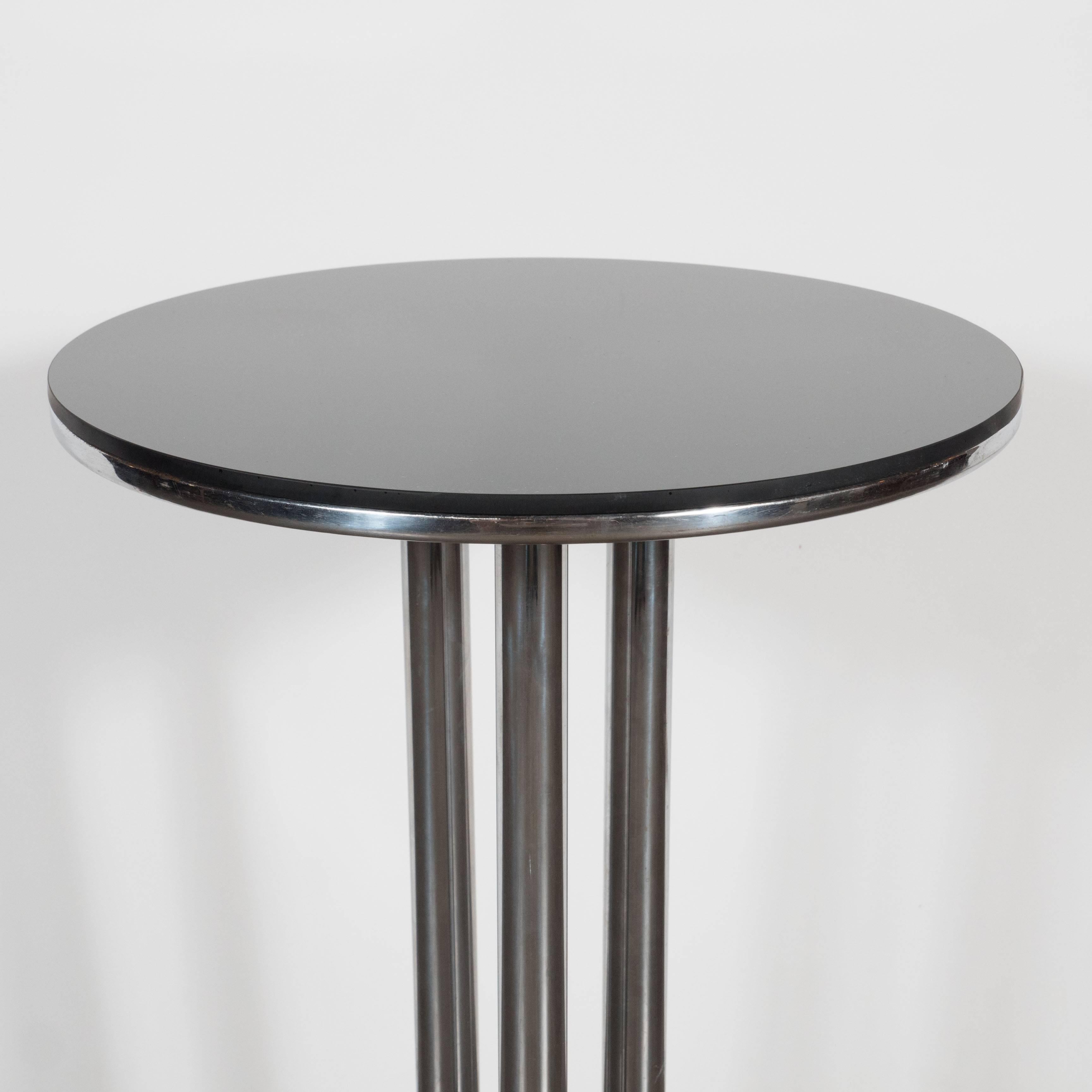 An Art Deco Machine Age drinks table in the manner of Donald Deskey featuring a column form stem on a skyscraper base in chrome and black enamel with a vitrolite top. A stylish versatile table that can be moved around with ease. An incredible