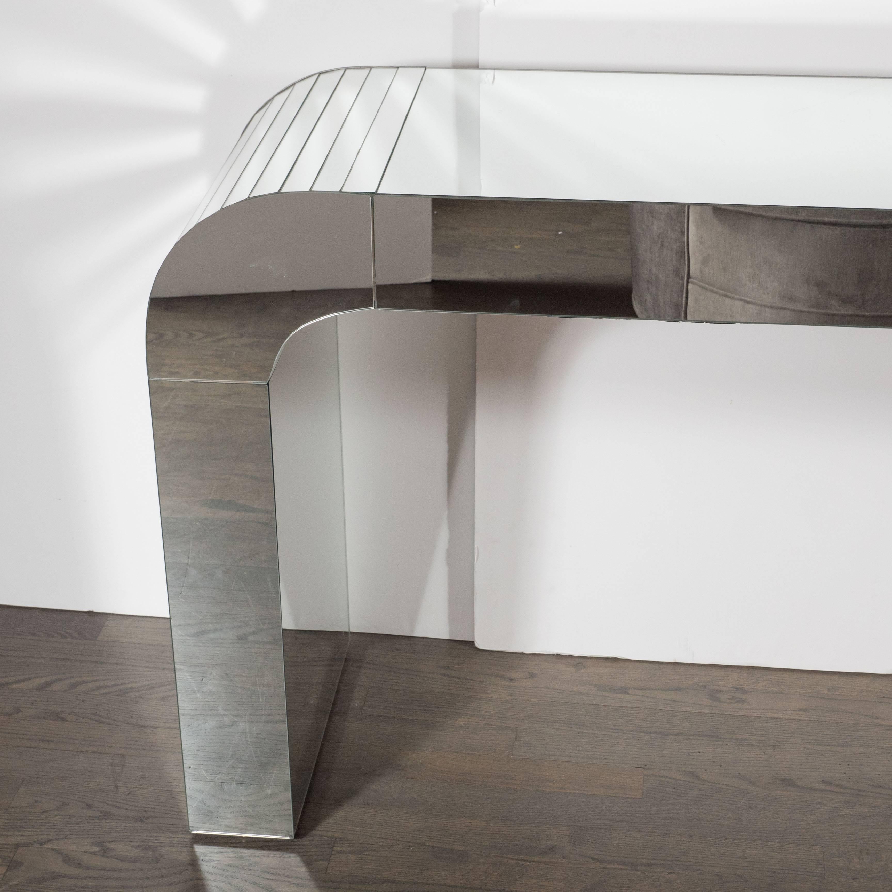 A Mid-Century Modernist arch form mirrored console table. A fully covered arch-form console is covered in segments of mirrored glass. This piece could also be used as a writing desk or vanity or console table. Its fully mirrored sides allow it to be