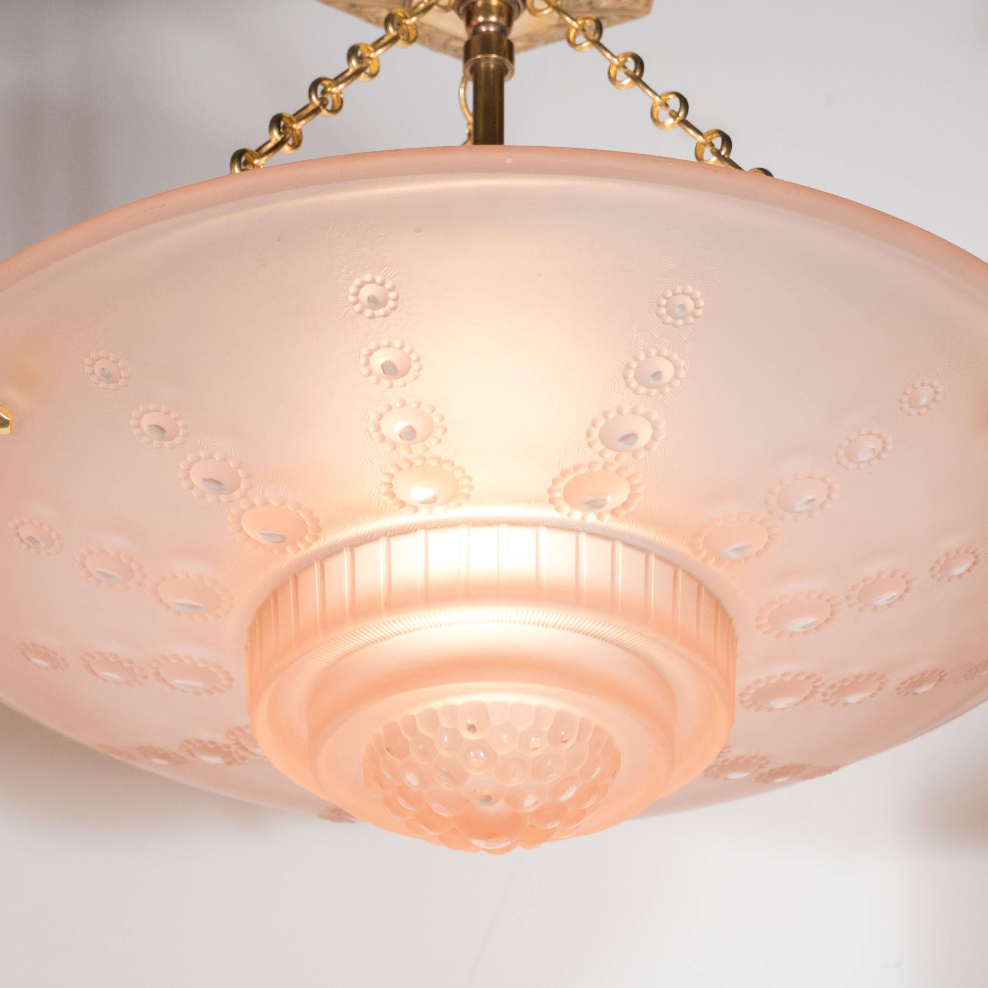 A French Art Deco inverted dome chandelier by Georges Leleu in frosted rose colored glass decorated with a repeated circular design ascending in size towards the center. It has delicate cross-hatch etching, beading and ridge detailing throughout.