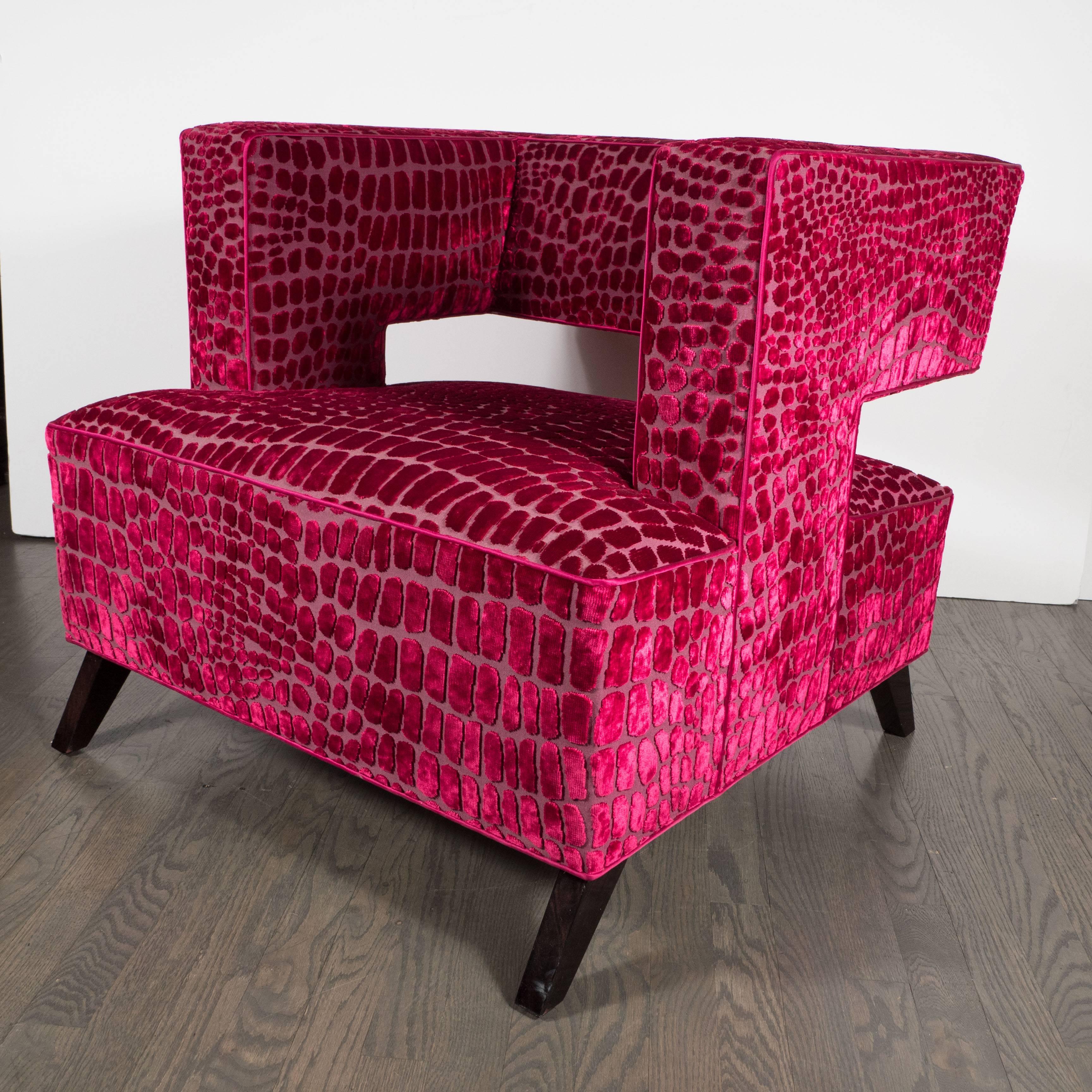 A pair of sculptural Mid-Century Modernist club or armchairs, a cubist design featuring strong angular lines, newly upholstered in a fuchsia croc Gauffraged velvet. They have a wraparound open-back and low profile, the tapered legs are ebonized