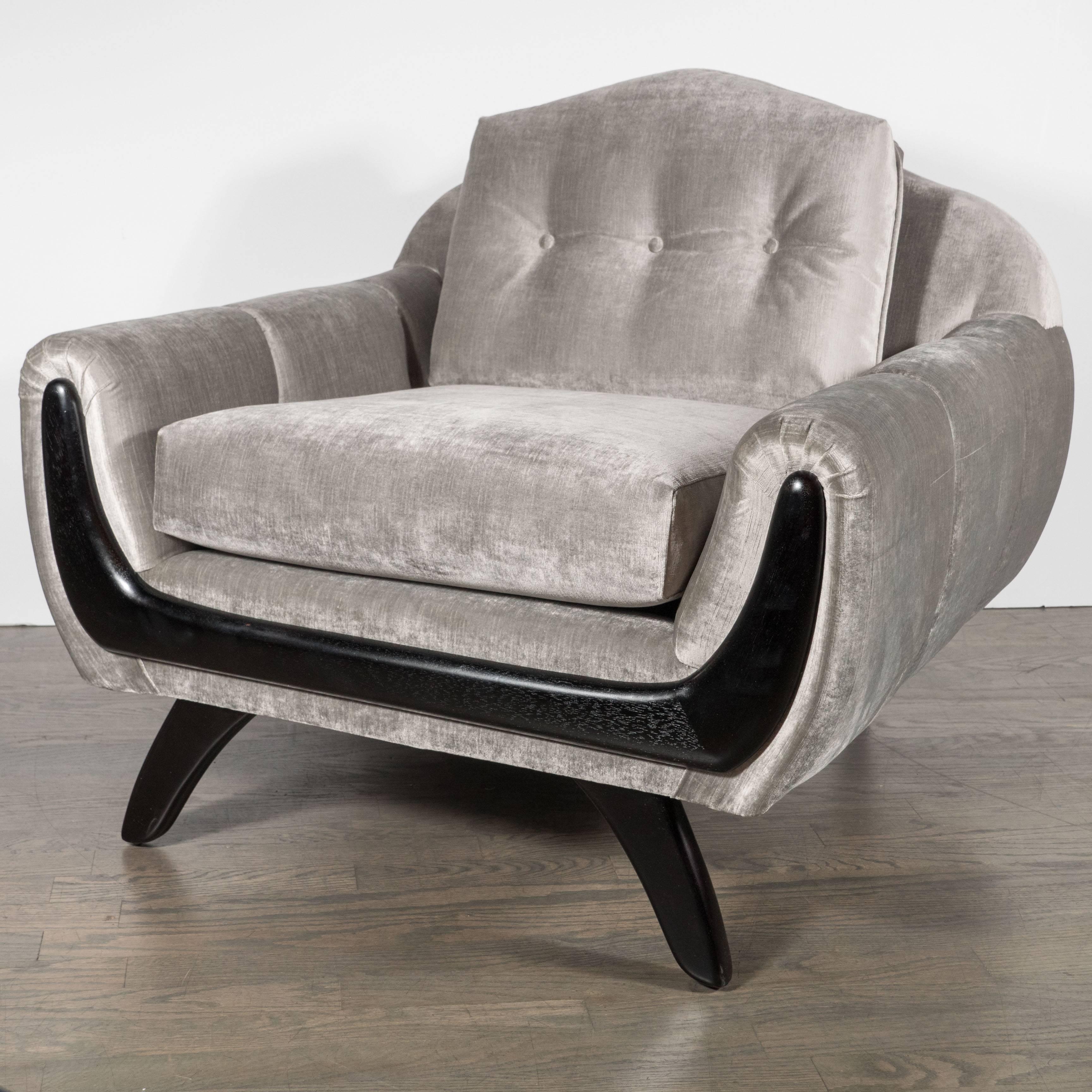 A pair of Mid-Century Modernist armchairs, low profile design with a hand rubbed walnut trim and splayed legs. These chairs are perfect for lounging and are extremely comfortable. They have been newly upholstered in a smoked platinum velvet and