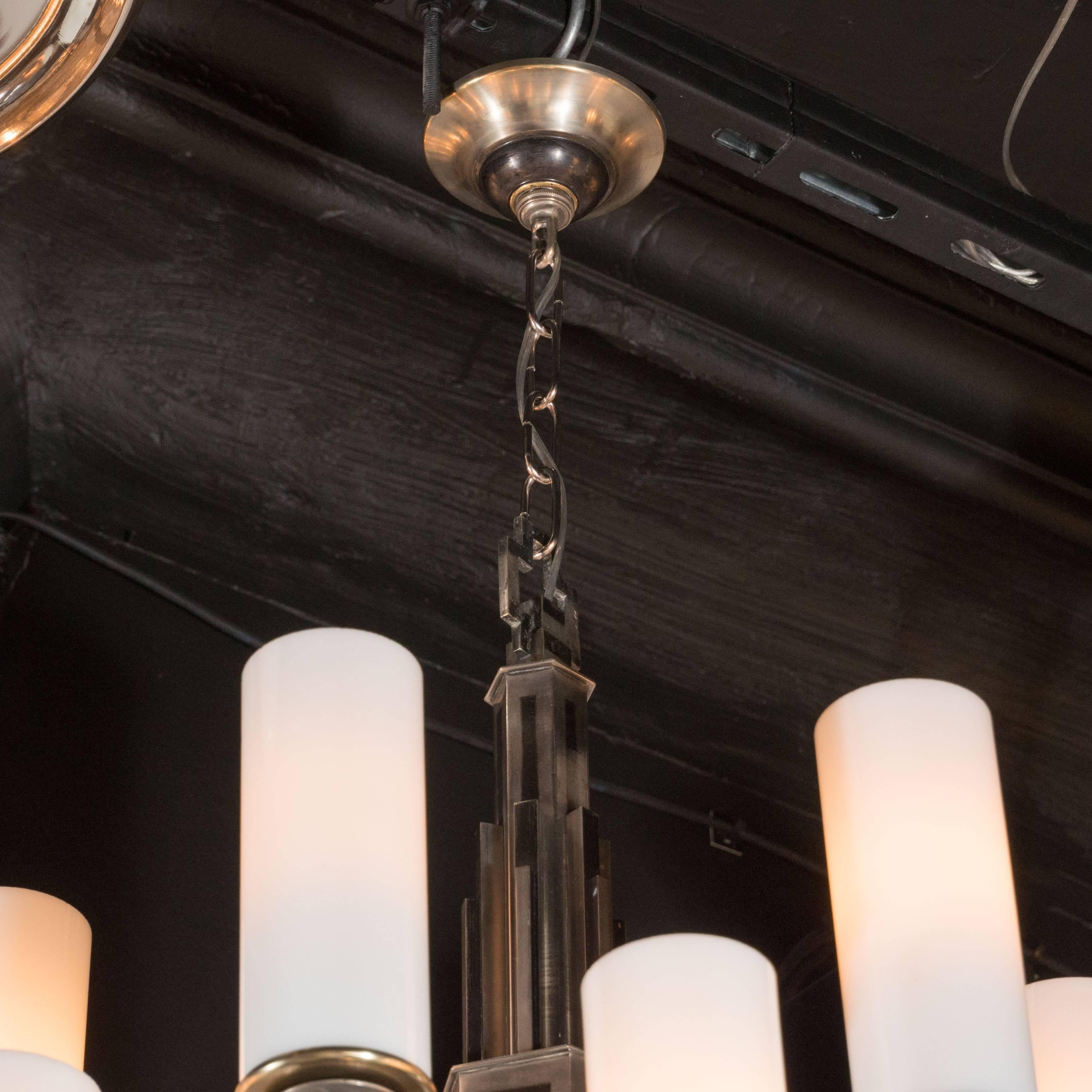 An exceptional Art Deco Machine Age chandelier, it consists of two tiers, each with six square tubular arms extending from an elaborate skyscraper style stem, each arm ends with a vertical cylindrical frosted glass shade with a brushed brass base.