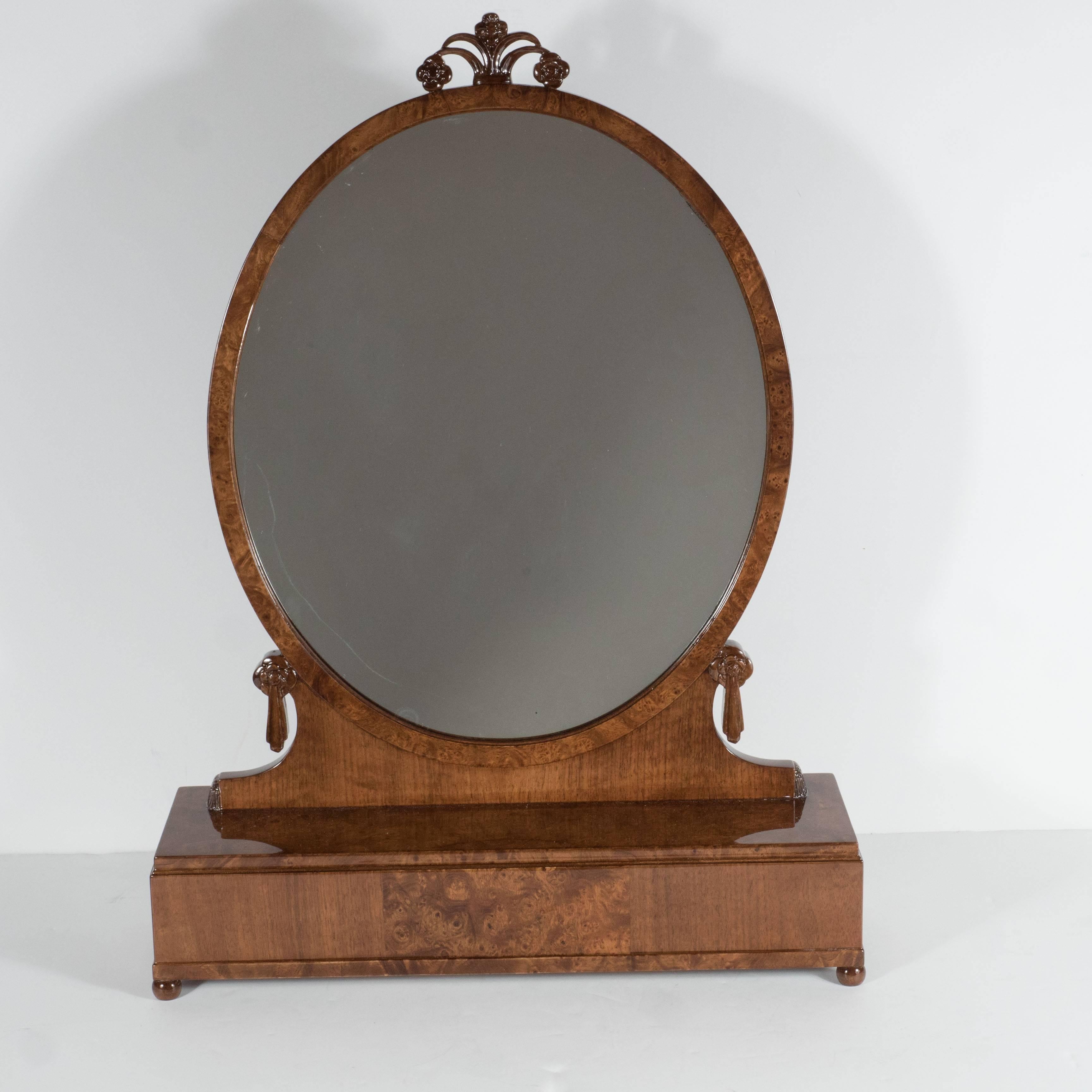This exquisite Art Deco book-matched exotic wood lady's top dresser mirror,was realized circa 1935 in the style of Jacques Emile Ruhlmann. It features Carpathian burled Elm and walnut hand-carved stylized foliate detailing. The oval shaped mirror is