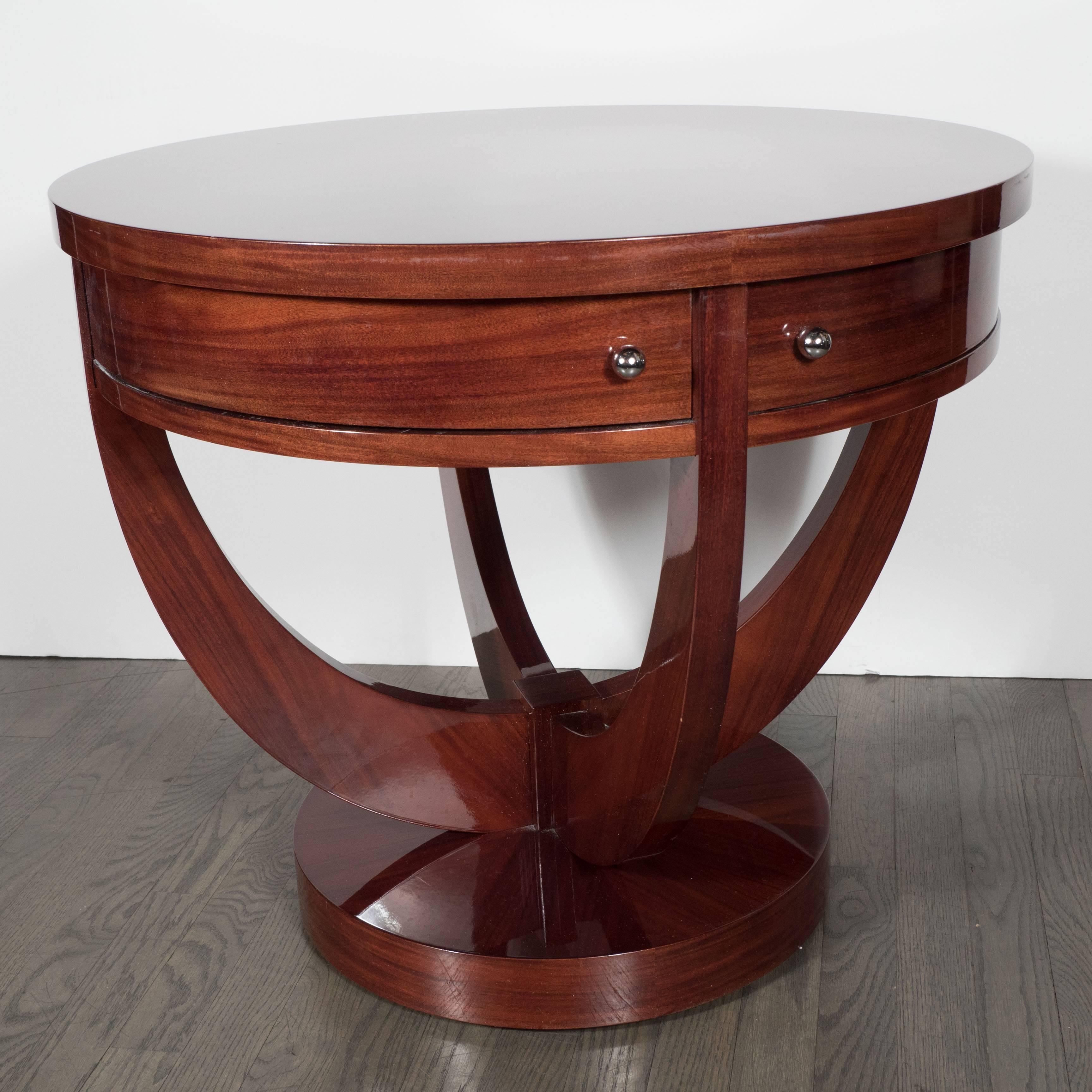 Art Deco gueridon compass-style table in book-matched mahogany. A circular base with four curved supports holds a table base which features four pie-shaped drawers, each fitted with a chrome ball pull. A beautifully book-matched, substantially sized