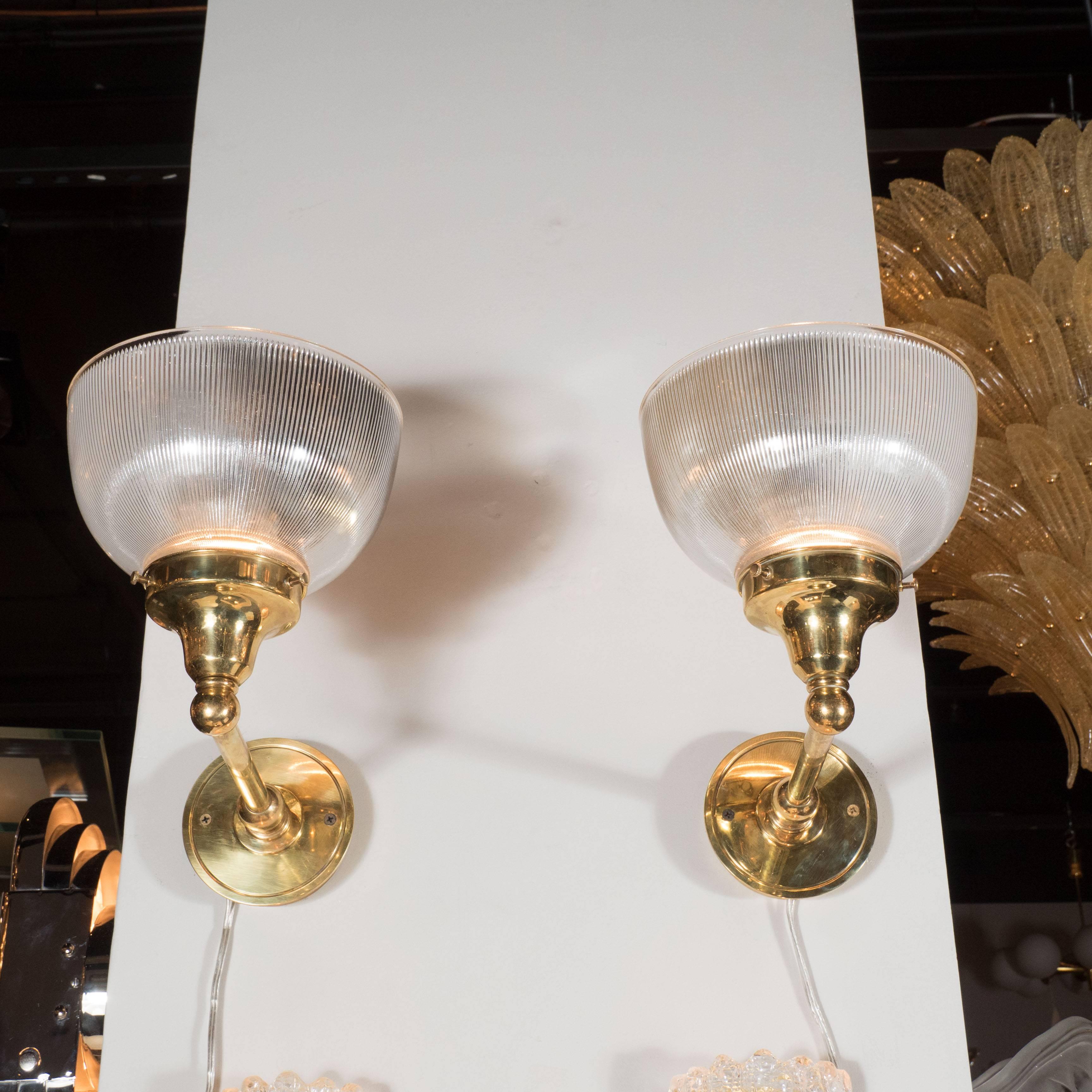These wonderful set of four sconces feature a reverse domed ribbed halothane glass shade with a polished brass arm with classical detailing. They have been newly rewired and are in excellent condition.
