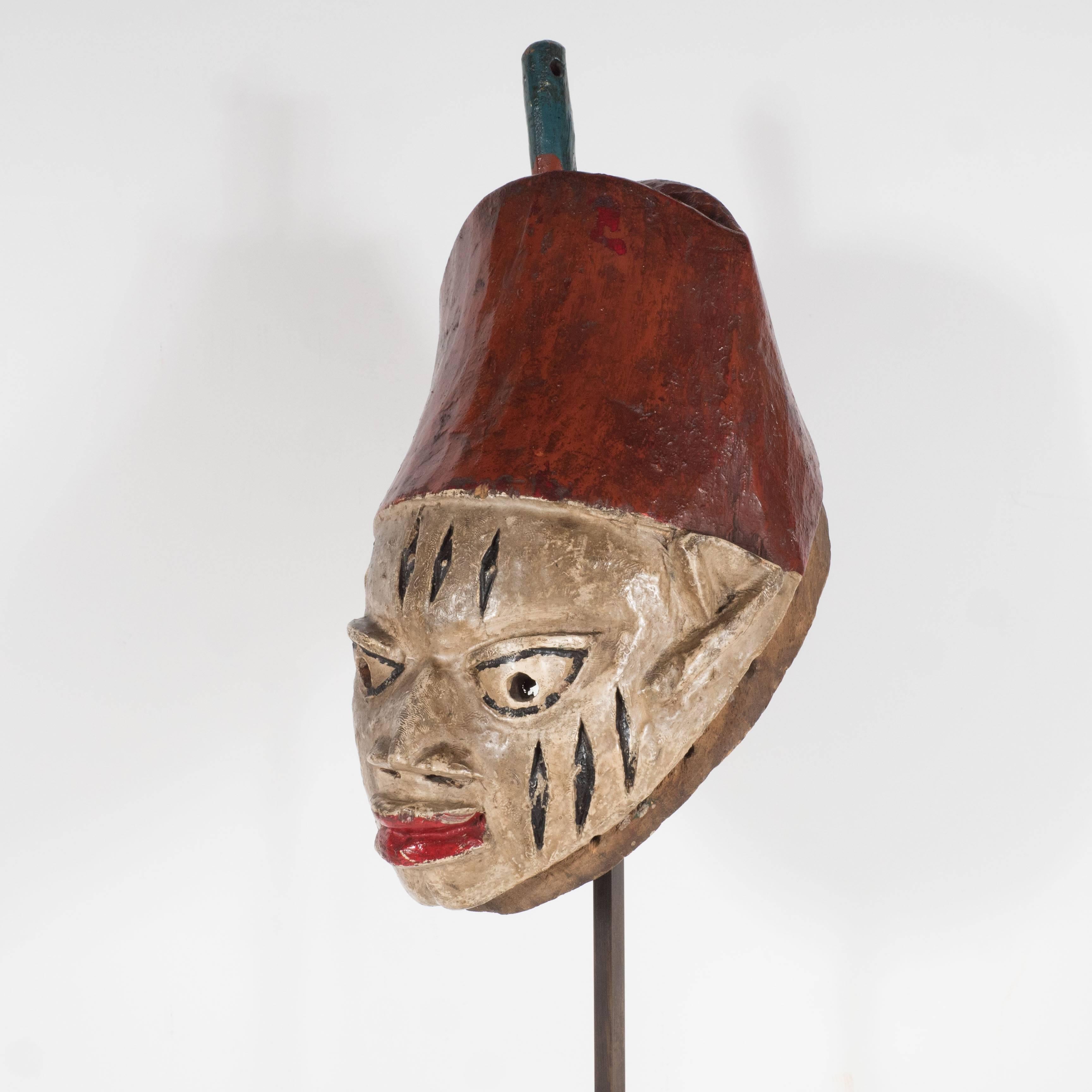 A painted head crest mask which appears to be from a 'Gelede cult,' known for honoring women and fertility, in the state of Benin (formerly Dahomey) in Nigeria, 20th century. This piece features vertical gash detailing on both cheeks and forehead. A