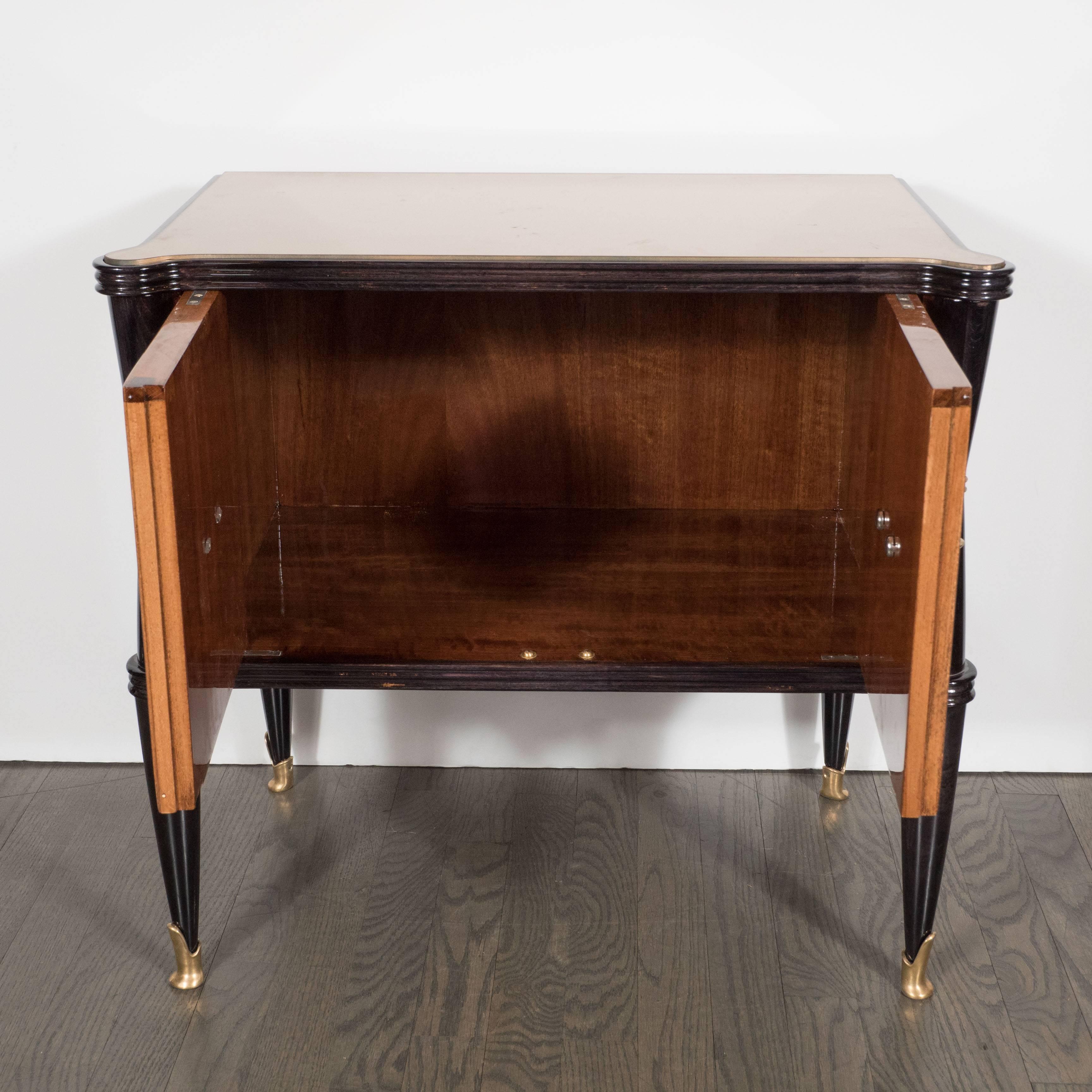 A pair of Mid-Century Modernist nightstands or end tables in rosewood with reversed painted gold mirror tops, gilt and brass detailing. 
Each with a pair of doors in beautifully grained rosewood and a stylish gilt and brass pull. The table tops
