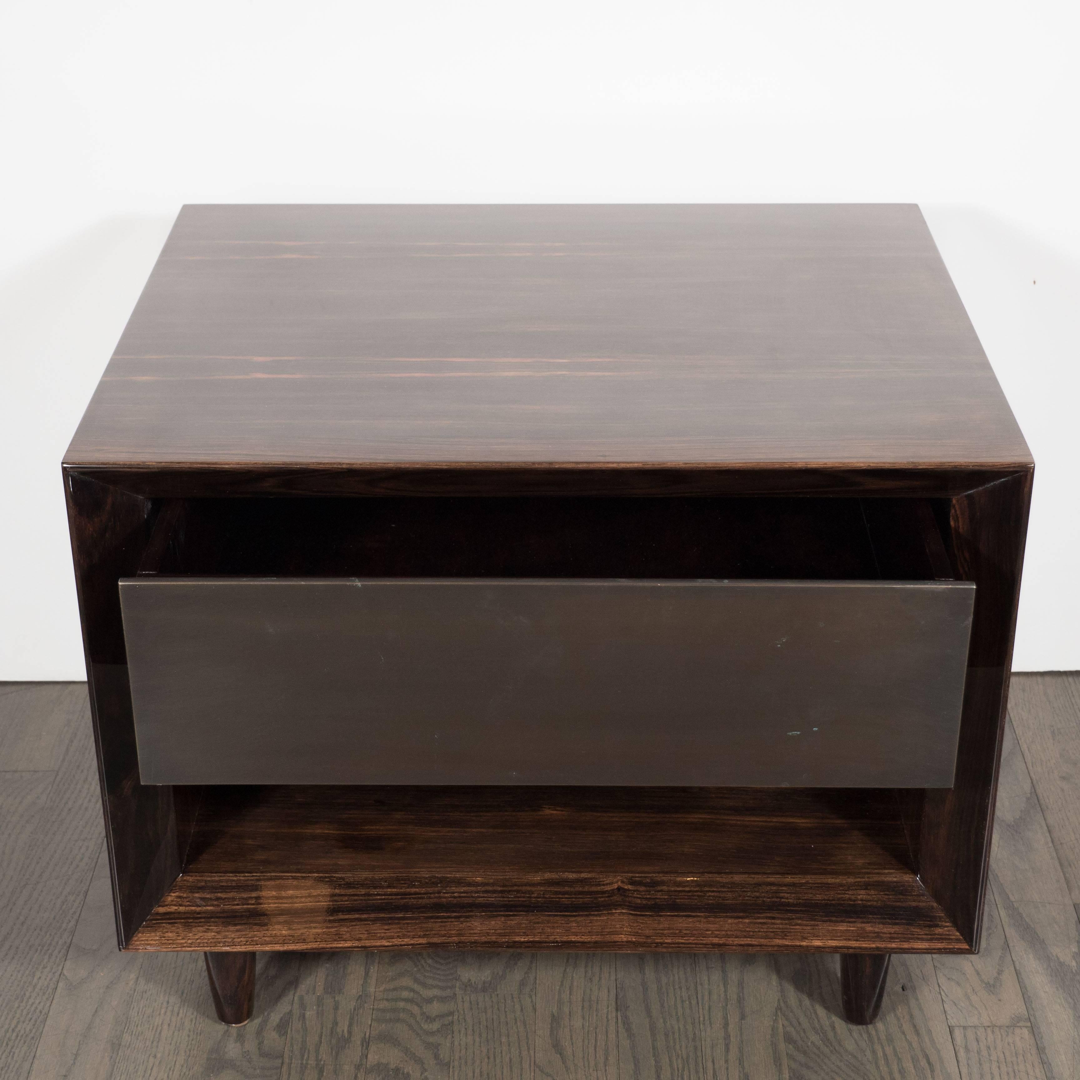 These stunning modernist nightstands feature a clean shadow box design in Macassar resting on four tapered legs with an open alcove area with a drawer above with front panel of bronze. These have been mint restored and in excellent condition.
These