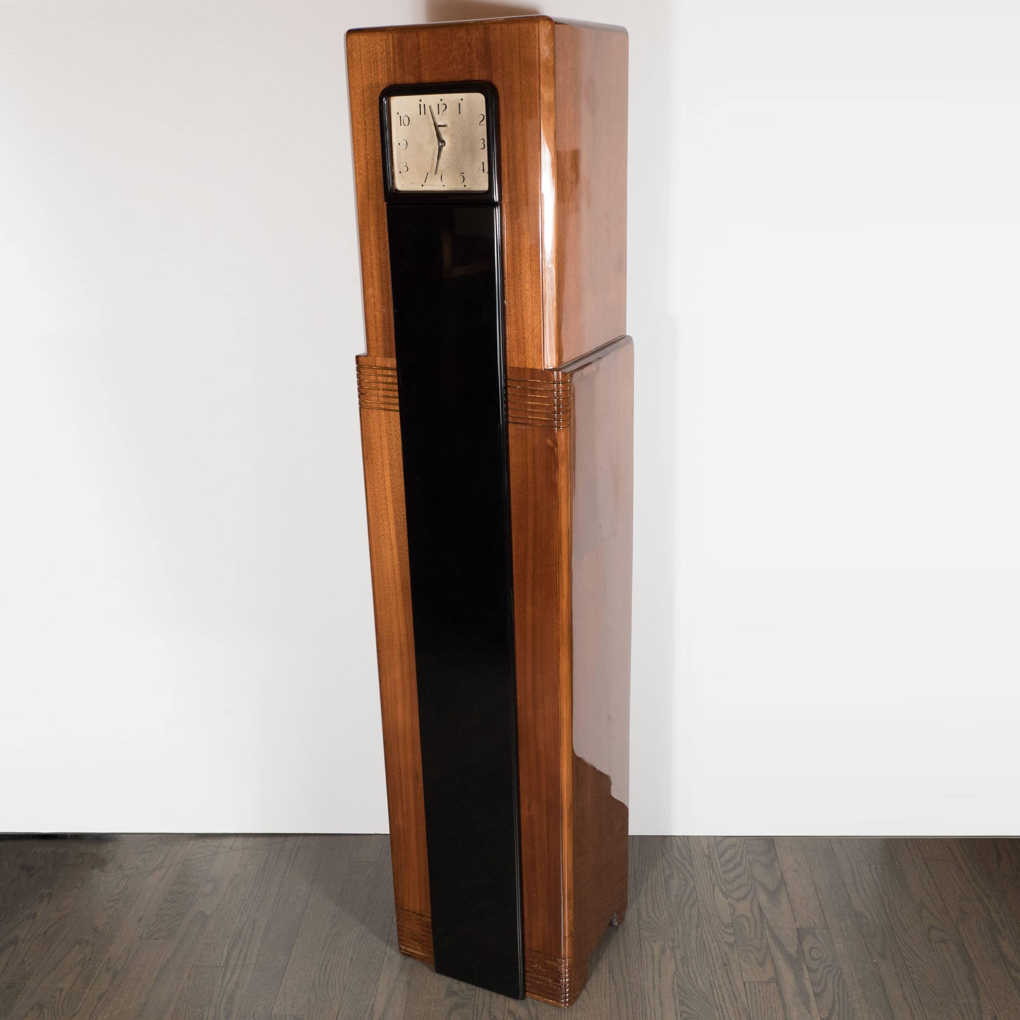 A streamlined American Art Deco skyscraper style grandfather clock in book-matched walnut and black lacquer, the streamlined clock case with typical linear recessed decoration in skyscraper style. 
The clockwork manufactured by famous Westinghouse,