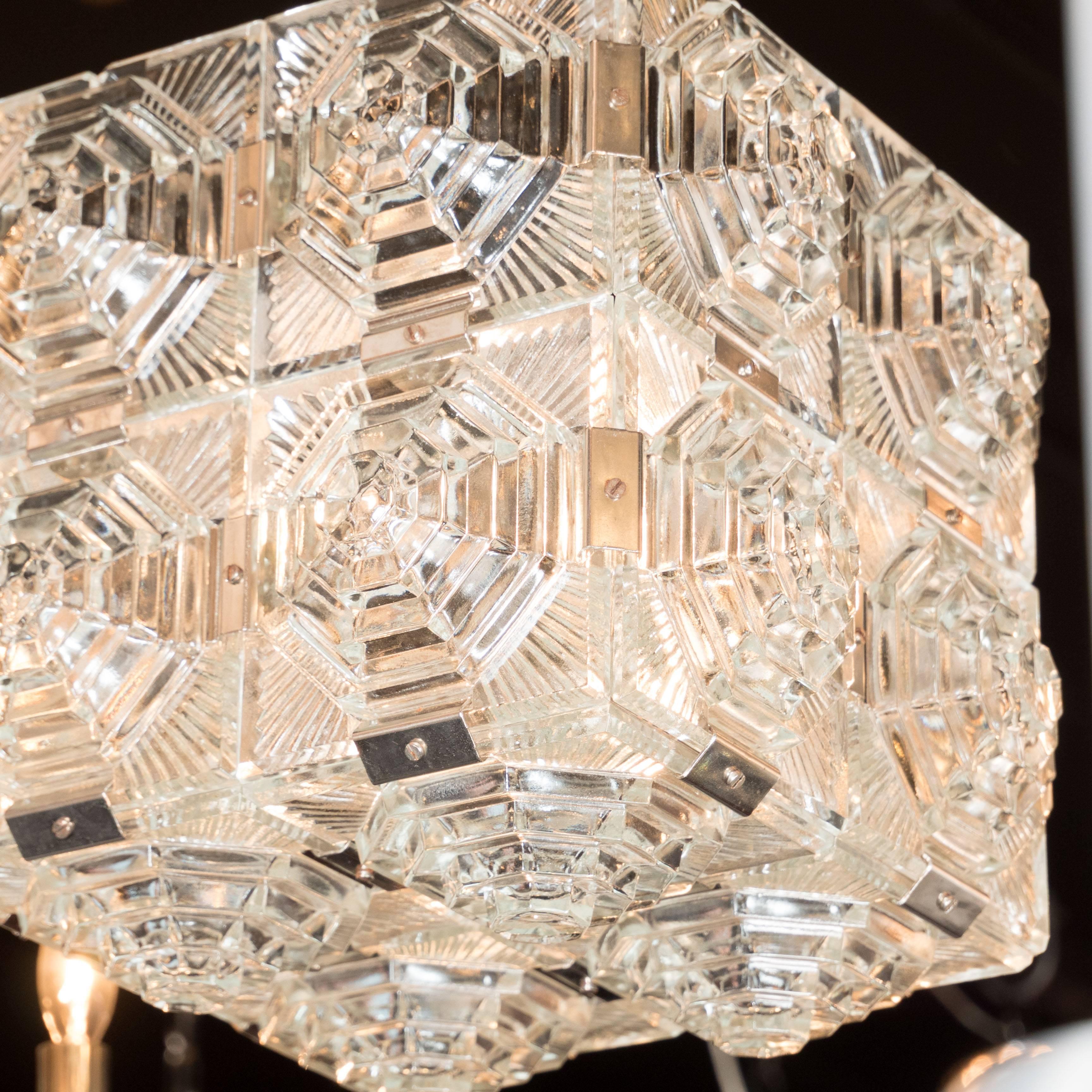 A Mid-Century Modernist pendant of textured glass panels with chrome fittings. Each side features four panels of etched glass featuring radial symmetry. Flat chrome connectors appear throughout. This piece hangs by a single rod and conical ceiling