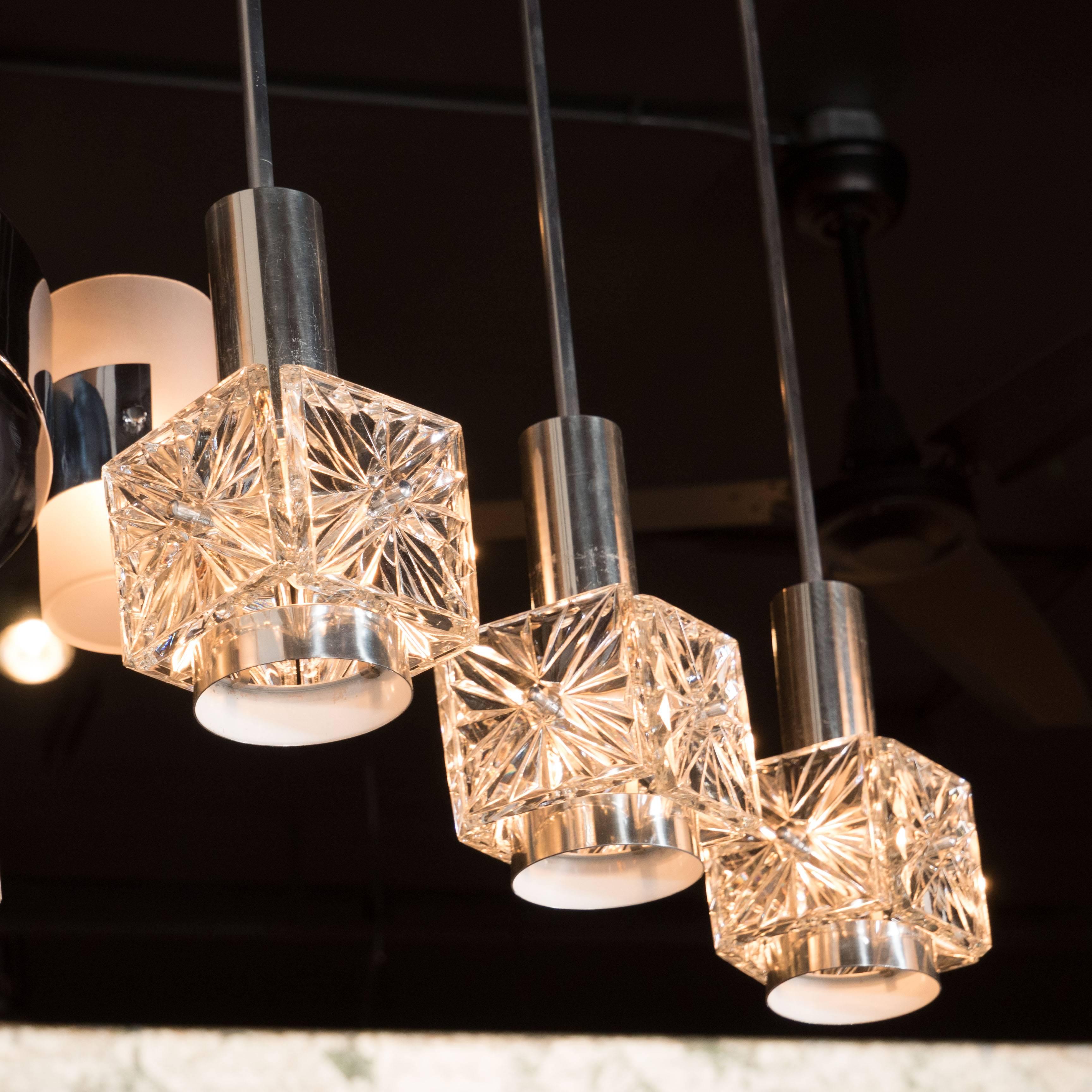 A set of three Mid-Century Modernist etched glass pendant chandelier in the style of Kinkeldy with chromed fittings. This chandelier features three downward hanging shades that each consist of faceted crystal squares with a hand-cut diamond pattern.