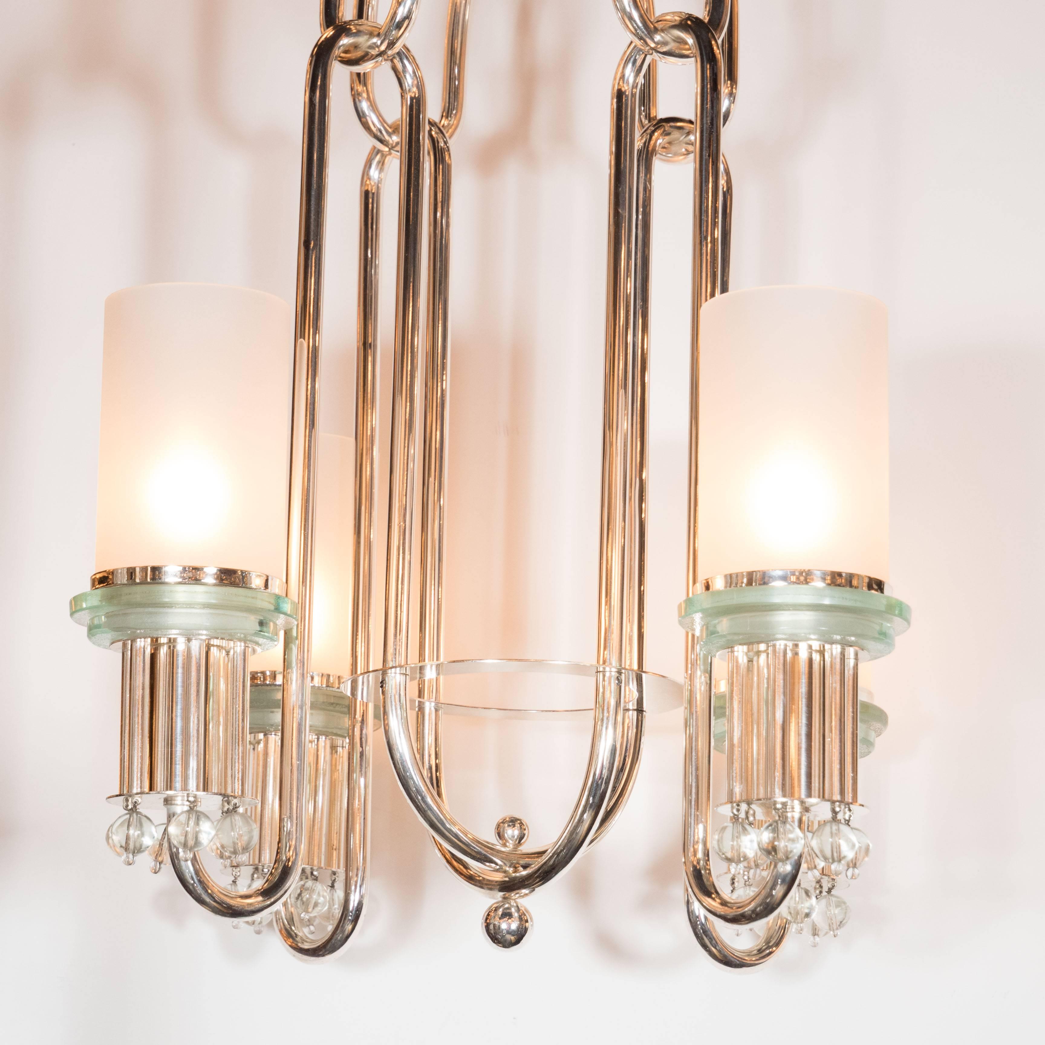 An elegant Art Deco nickeled bronze sculptural chandelier with cylindrical frosted glass shades, France, circa 1930.
This machine age inspired chandelier features four frosted cylindrical glass shades on a stepped frosted cylindrial glass support,