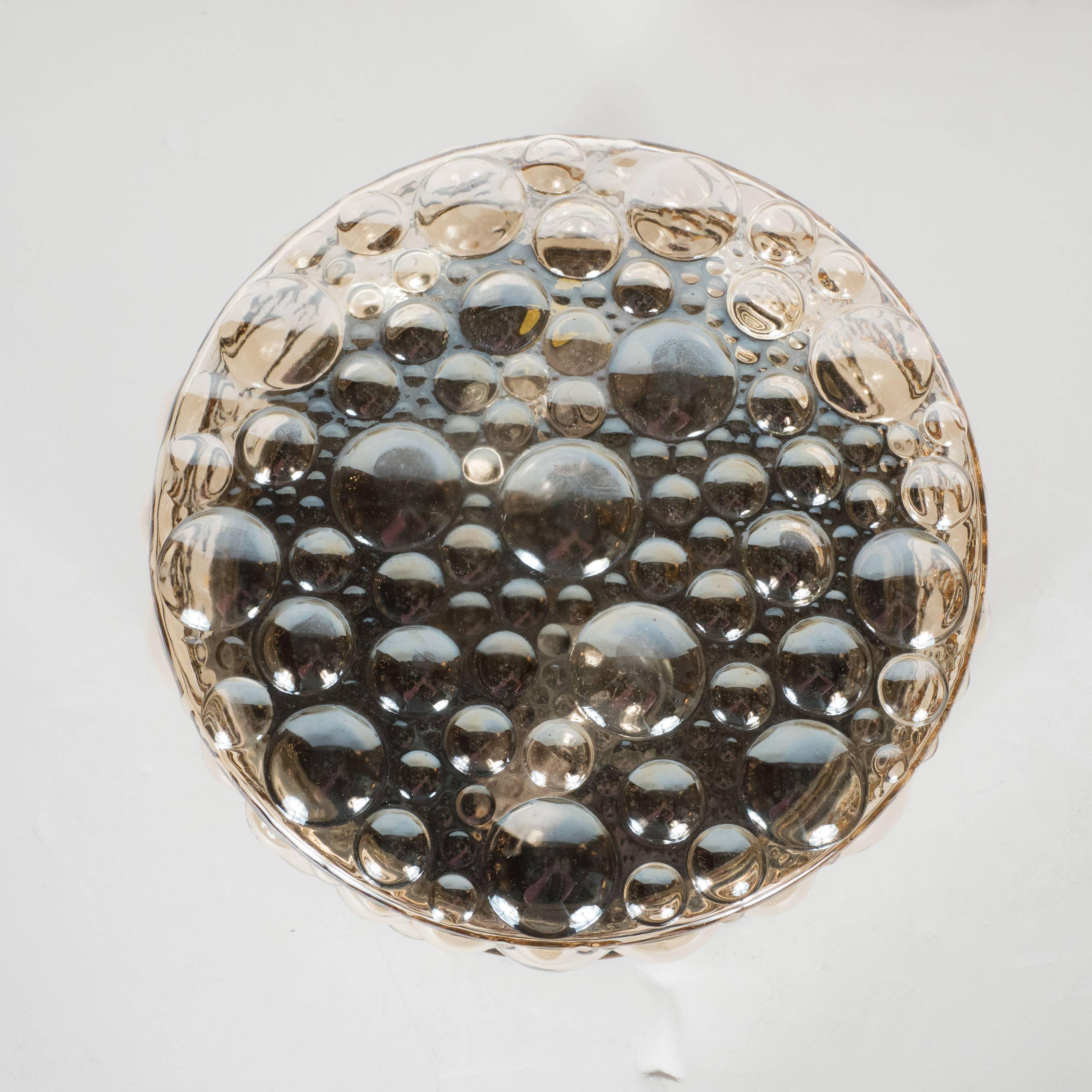 A Mid-Century Modernist textured bubble glass flush mount chandelier with antiqued brass fittings. A single, stepped detail antiqued brass ring supports a disc-shaped, textured smoked glass shade, adorned with outward protruding bubbles in various