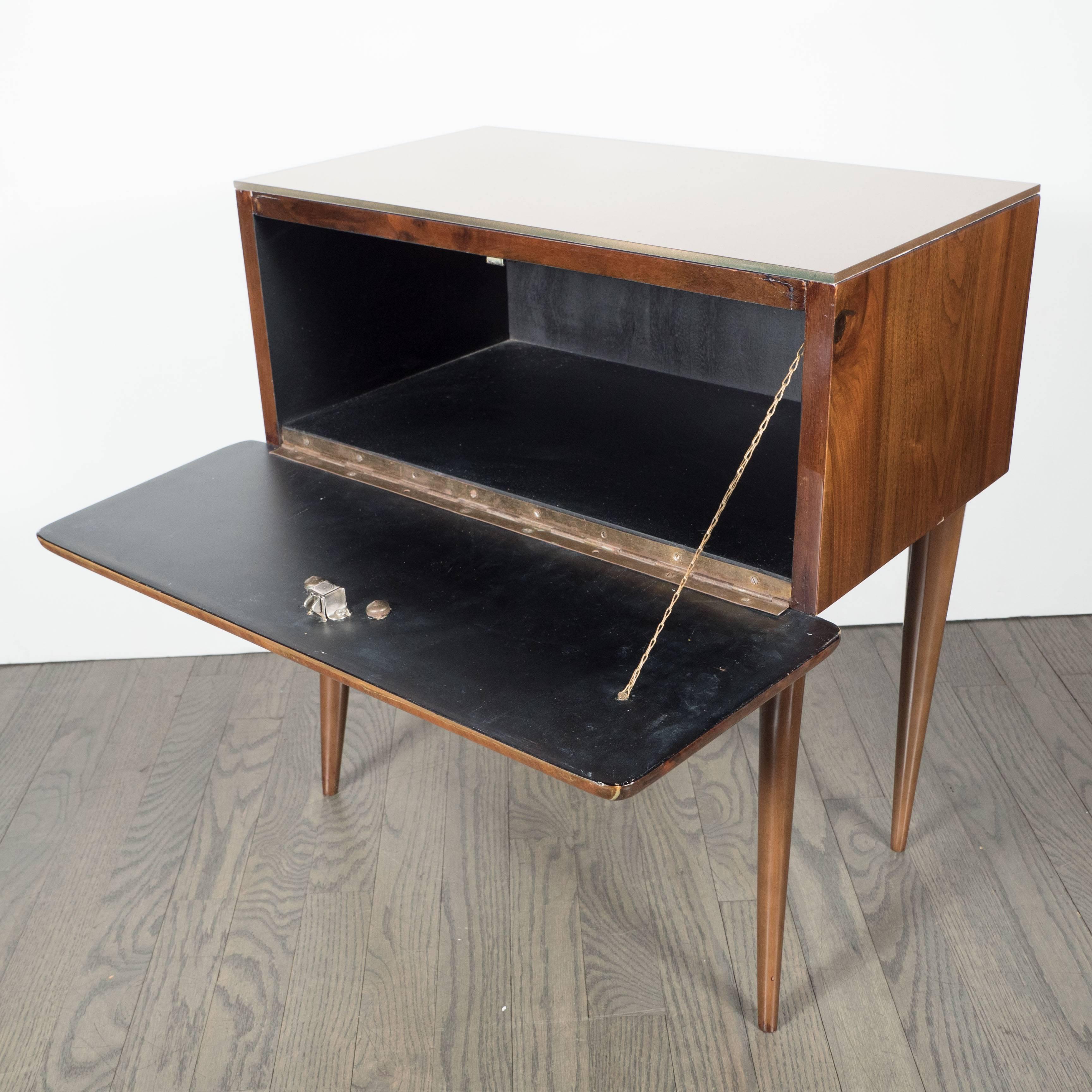 Sophisticated nightstand or end table features a drop front drawer with bookmatched inlays of burled walnut and zebra wood with a holly inlay and a clean modernist handle in the center. The top features a reverse églomisé gold painted glass top. The