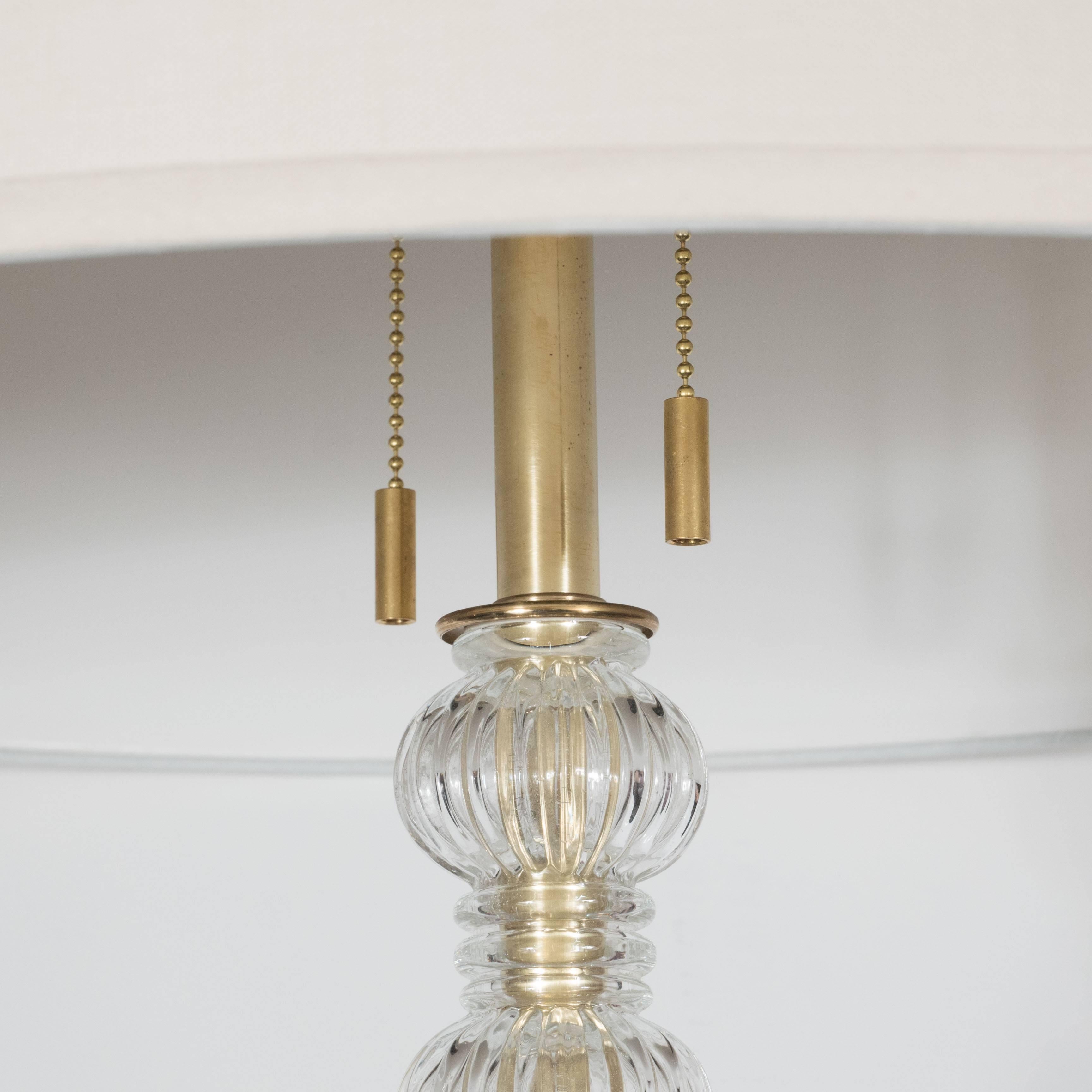Mid-century Modernist floor lamp in Murano glass and brass, on a simple yet elegant circular base, the sleek brass stand beautifully interspersed with delicately molded Murano glass elements, two fittings with chains fitting two Edition bulbs,