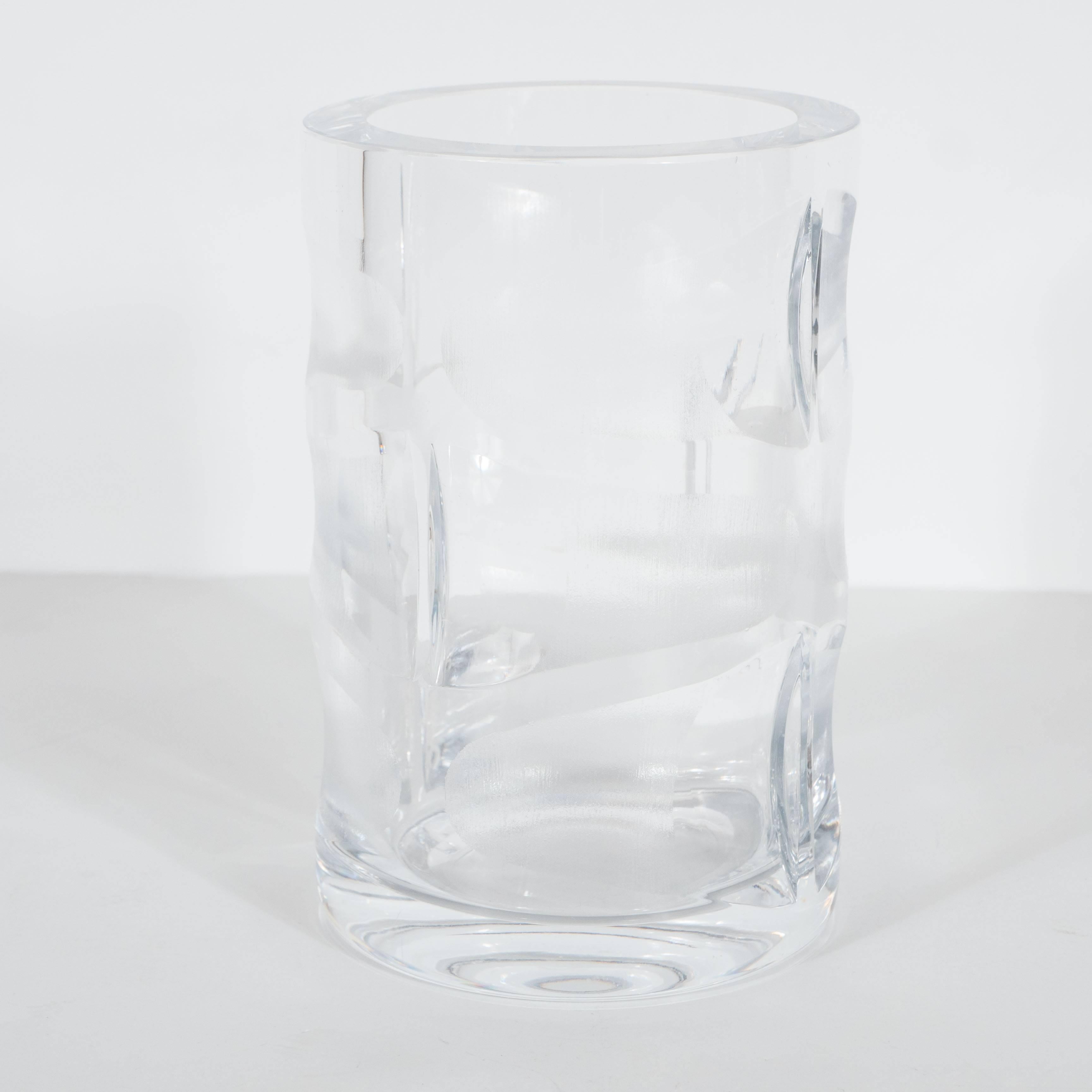 
This Mid-Century Modernist crystal vase in clear glass features geometric designs in clear and etched glass. It was realized, circa 1970, in the style of Orrefors of Sweden. Photographs do not do the subtle finishes of this sophisticated vase