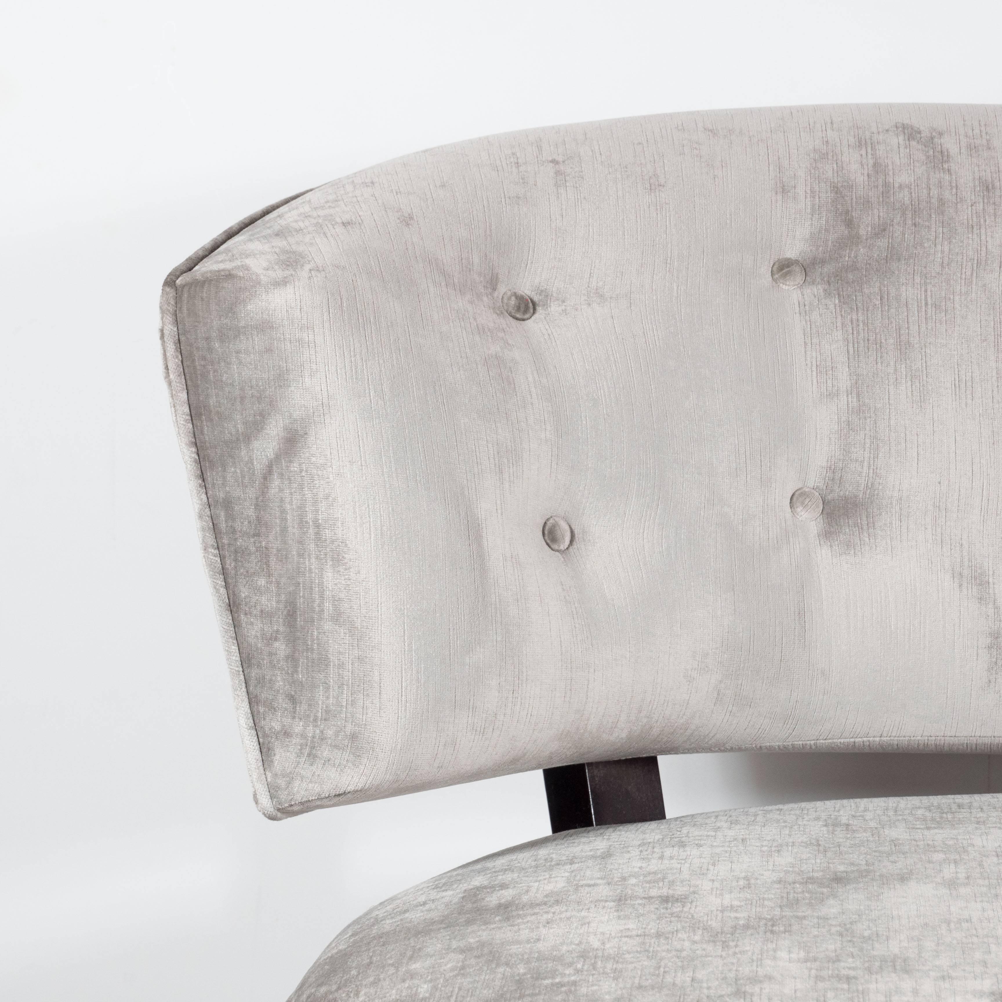 A pair of Art Deco rounded slipper chairs in smoked platinum velvet by Gilbert Rohde. Conical feet in ebonized walnut support bulbous, fully upholstered seats, which connect to curved, tufted seat-backs. Newly upholstered in a luxe platinum velvet