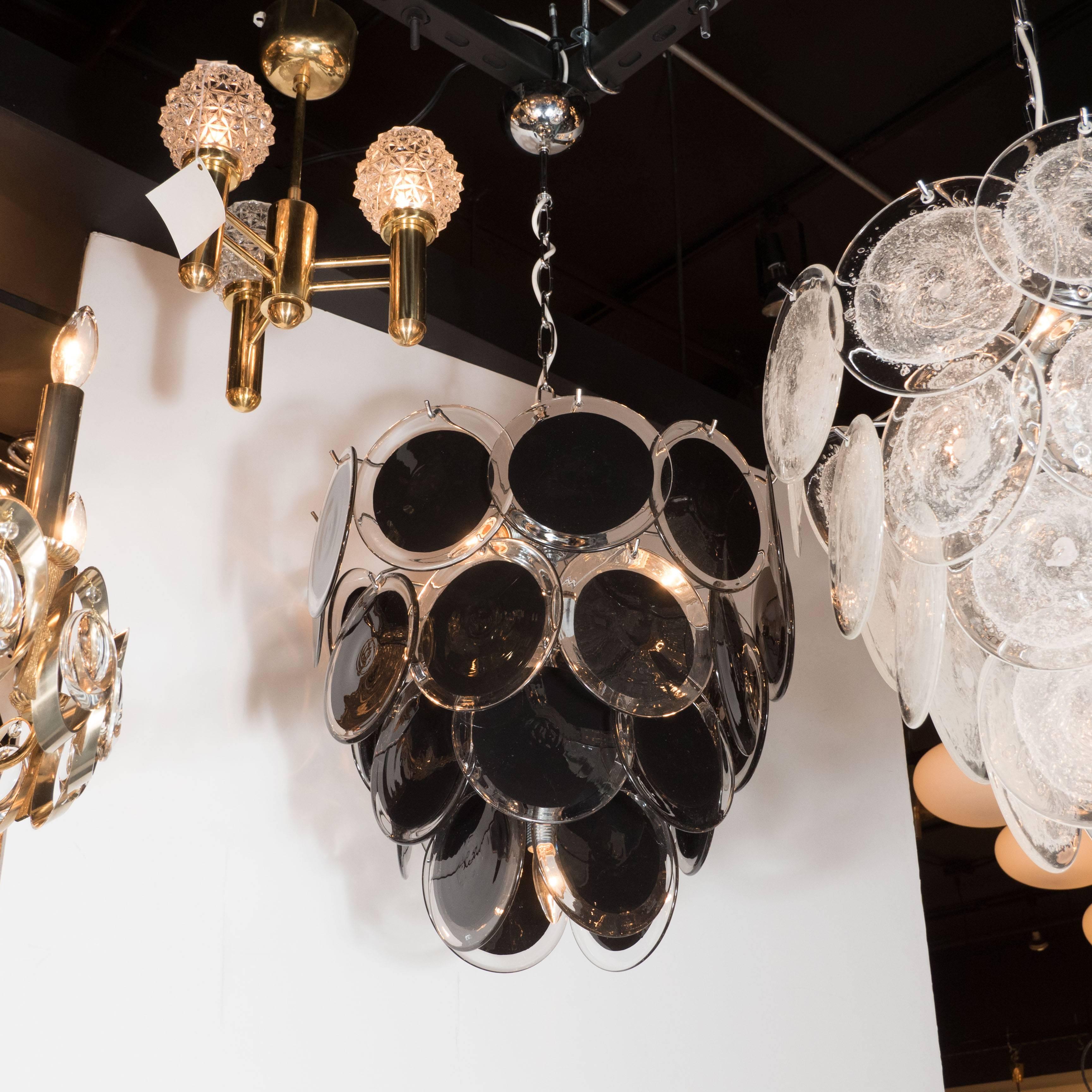 This Modernist chandelier, in the manner of Vistosi, features 36 individually suspended black discs with clear rims in handmade Murano glass. Collectively, the discs offer a cascading four tiered design. With its forward thinking, yet incredibly