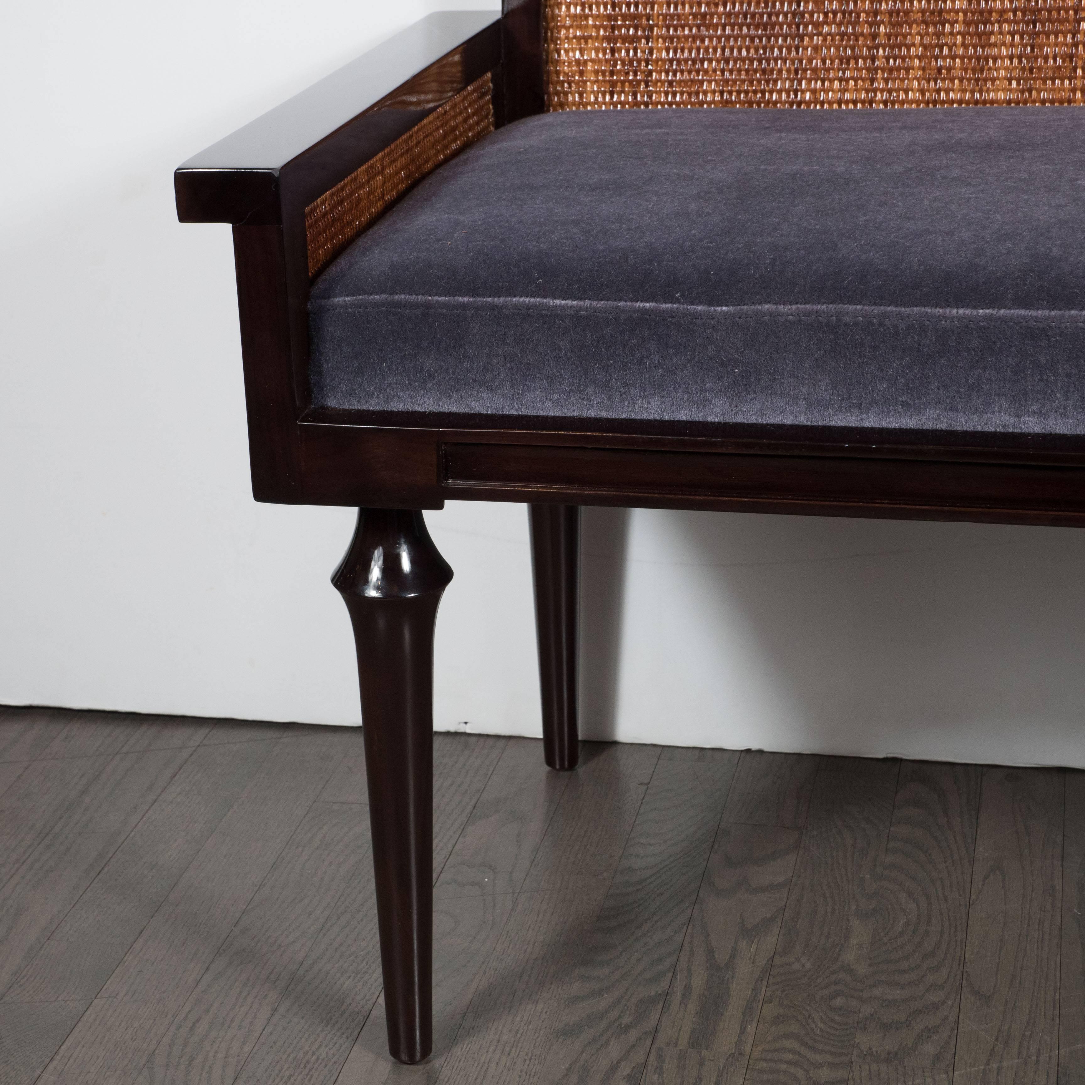 A Mid-Century modernist bench or settee in ebonized walnut with inset stained caning a smoked amethyst mohair. Conical legs support a clean, Minimalist frame. Flat armrests protrude from each side. A low-back features two panels of caning. Newly