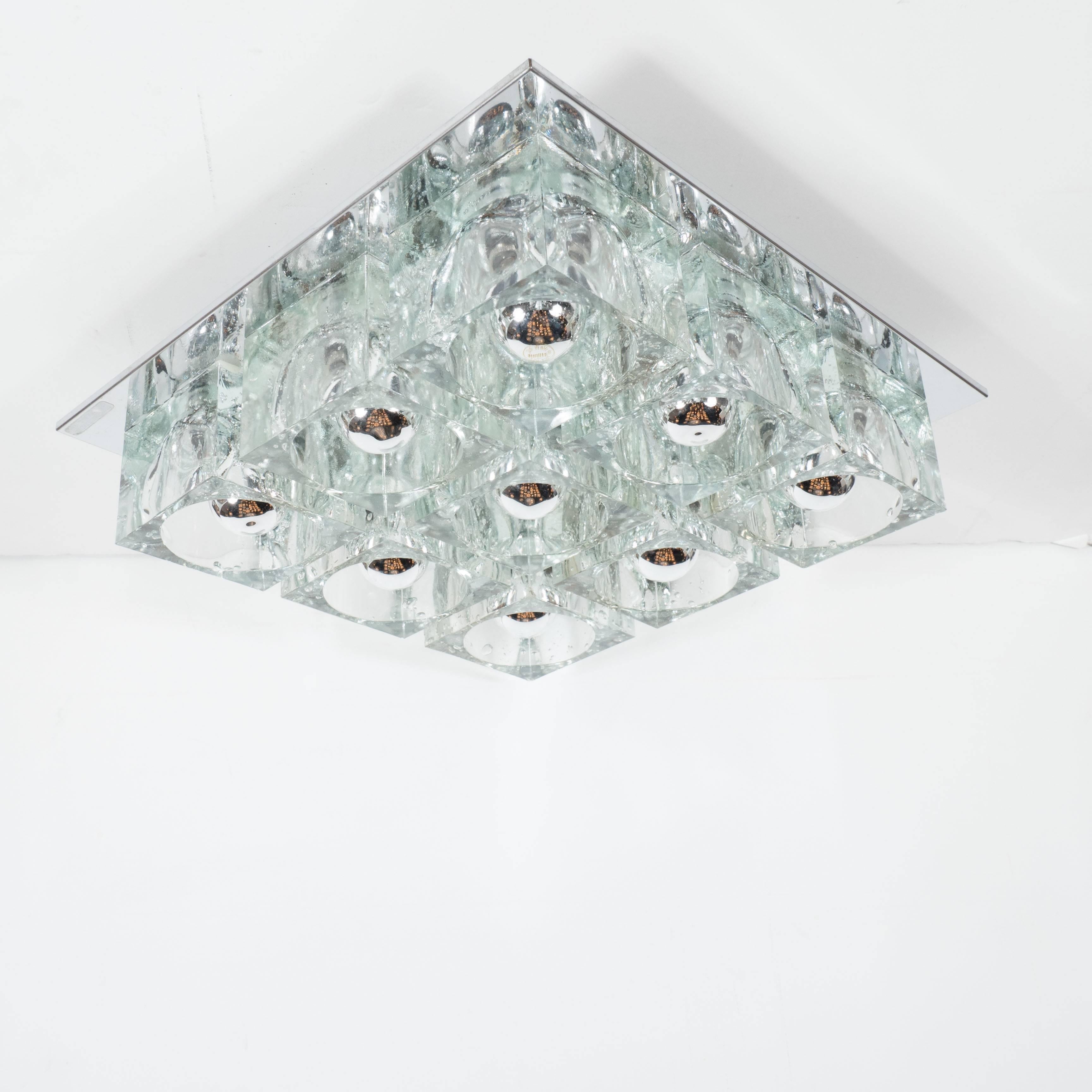 This brilliant Mid-Century Modern flush mount chandelier by Sciolari features nine thick clear glass cubes with inset bulbs fixed to a close fitting chrome backplate. The design has strong geometric qualities with the cubes of the glass strongly