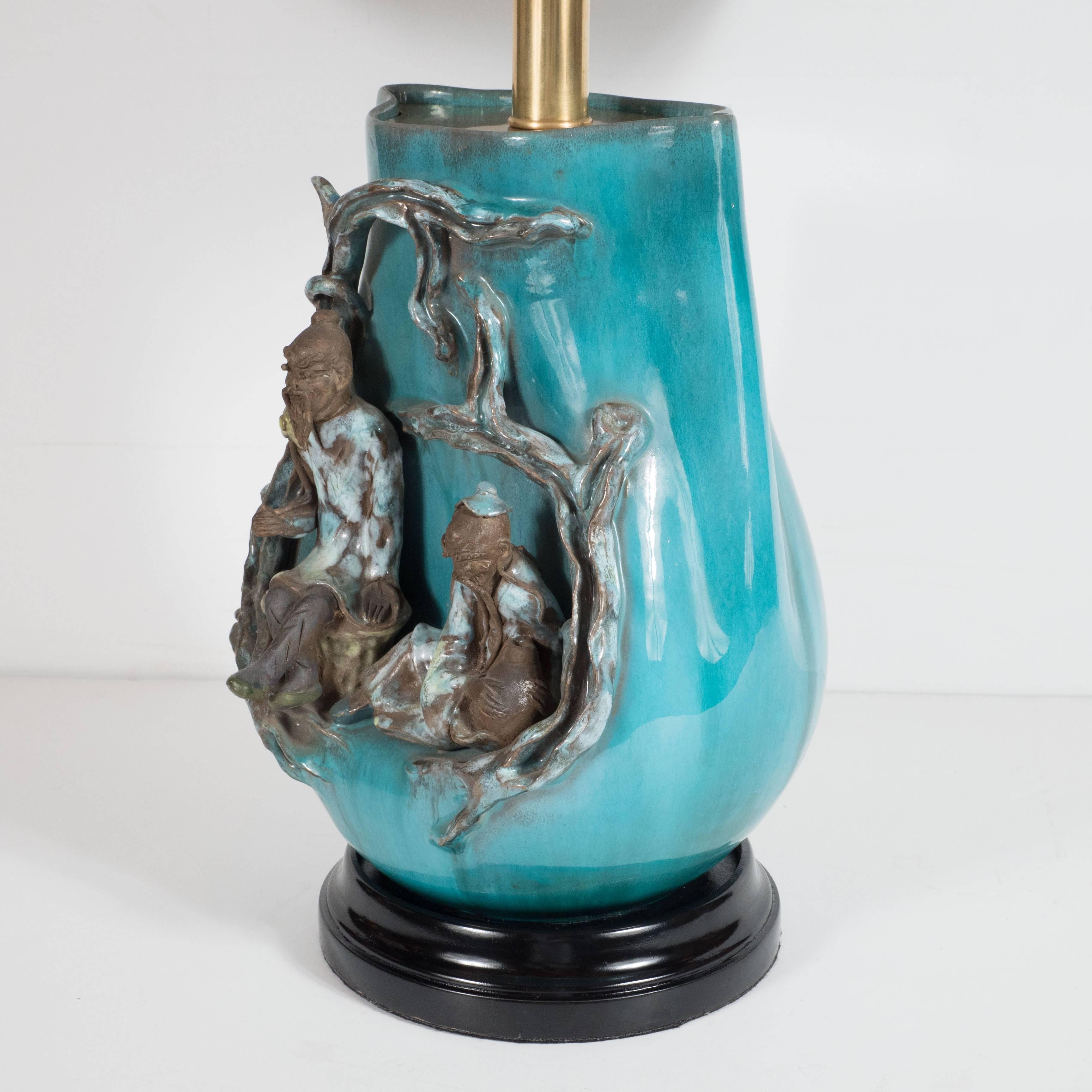 Moderne Tischlampe von Marcello Fantoni aus reich glasiertem, leuchtend türkisblauem Steingut in Vasenform, aufwändig verziert mit zwei unter einem Baum sitzenden Weisen, das Ganze auf einem ebonisierten, gestuften Holzsockel, über einem auffallend