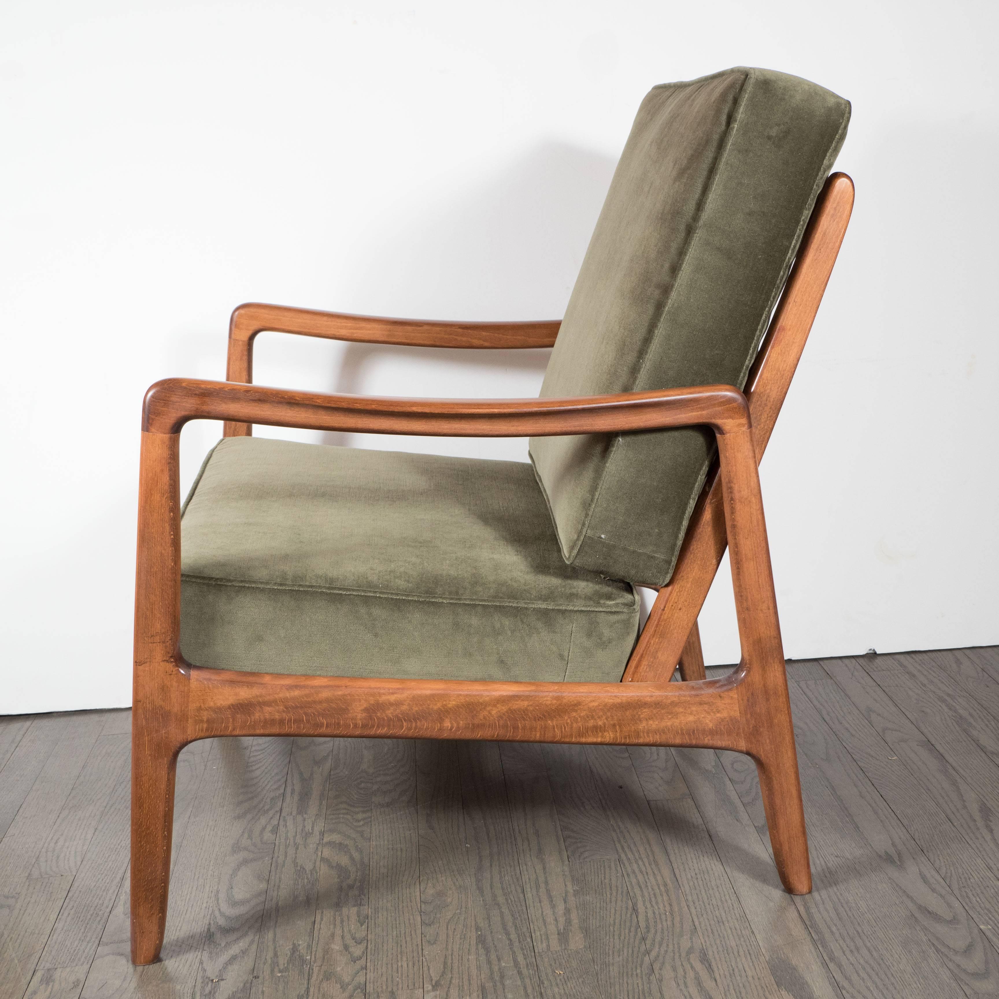 A Mid-Century Modern hand-rubbed walnut armchair in sage velvet. A sturdy walnut frame with slightly sloped armrests and rounded edges supports two removable cushions newly upholstered in a warm smokey sage velvet upholstery. A simple and elegant