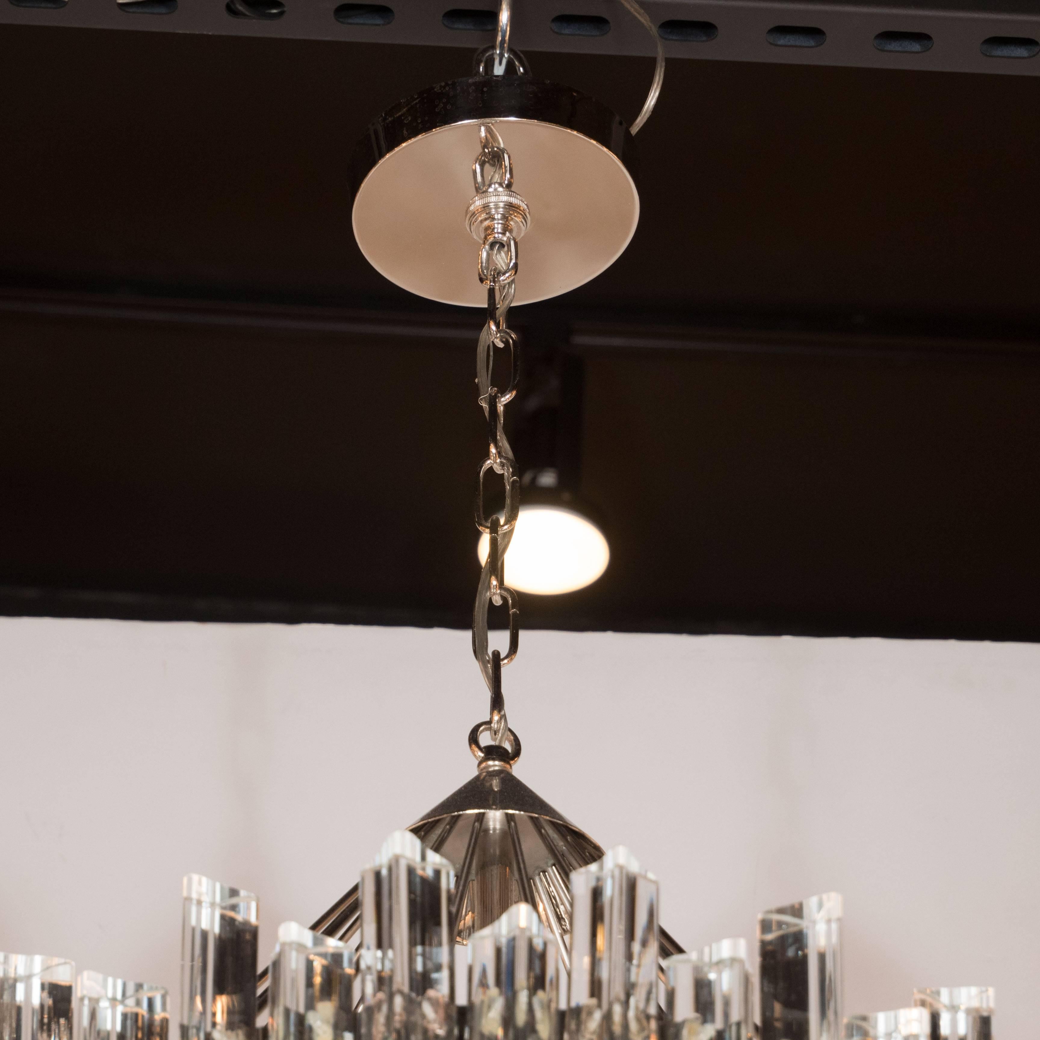 A Mid-Century modernist single-tier stepped triedre chandelier by Camer. A chrome birdcage-frame fitted with a single Edison-based socket surrounded by individually hung crystal triedre prisms in a staggered manner. The overall hanging height can be