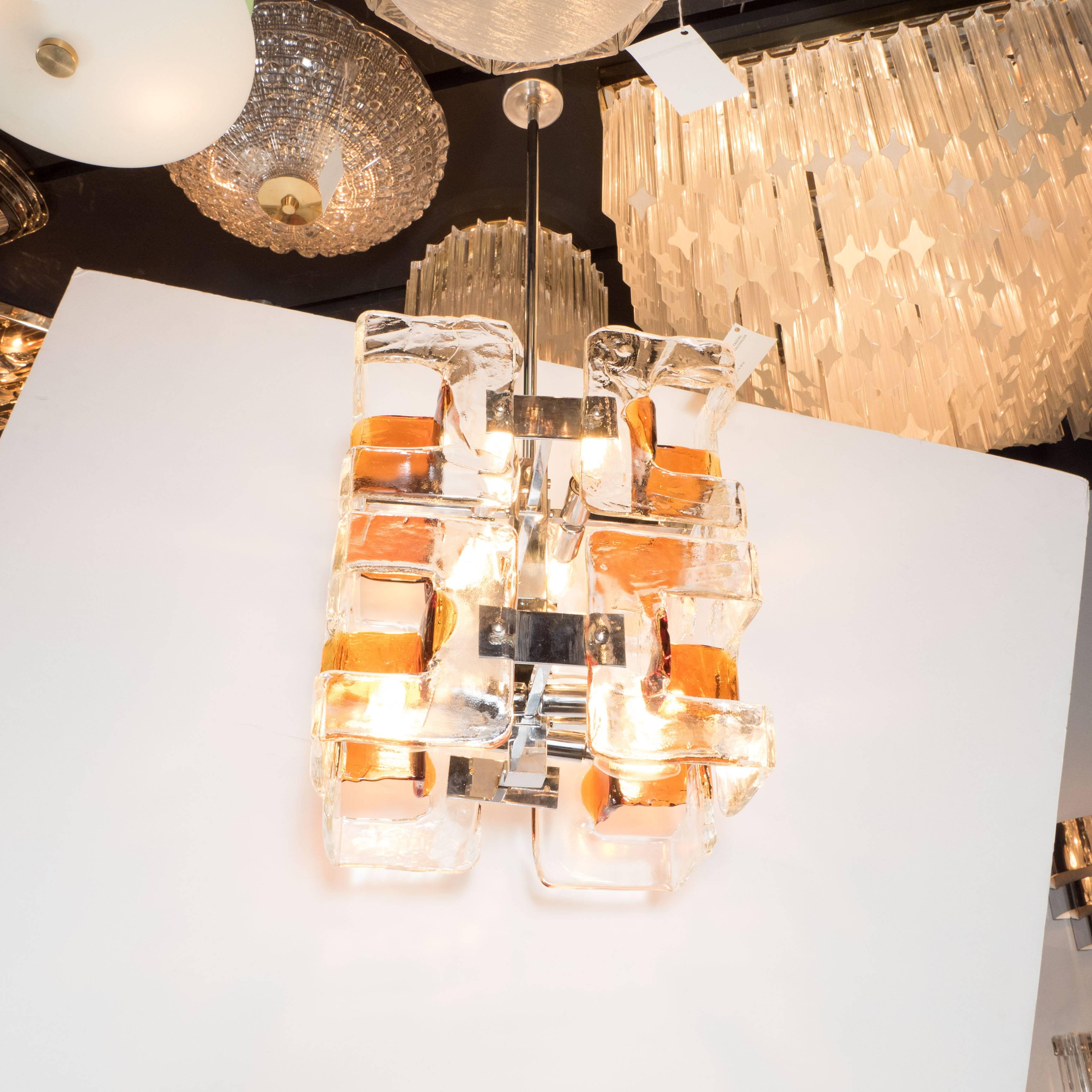 This dramatic and elegant Mid Century Modern chandelier was realized in Murano, Italy- the island off the coast of Venice renowned for centuries for its superlative glass production- by the fabled lighting atelier Mazzega circa 1970. It offers a