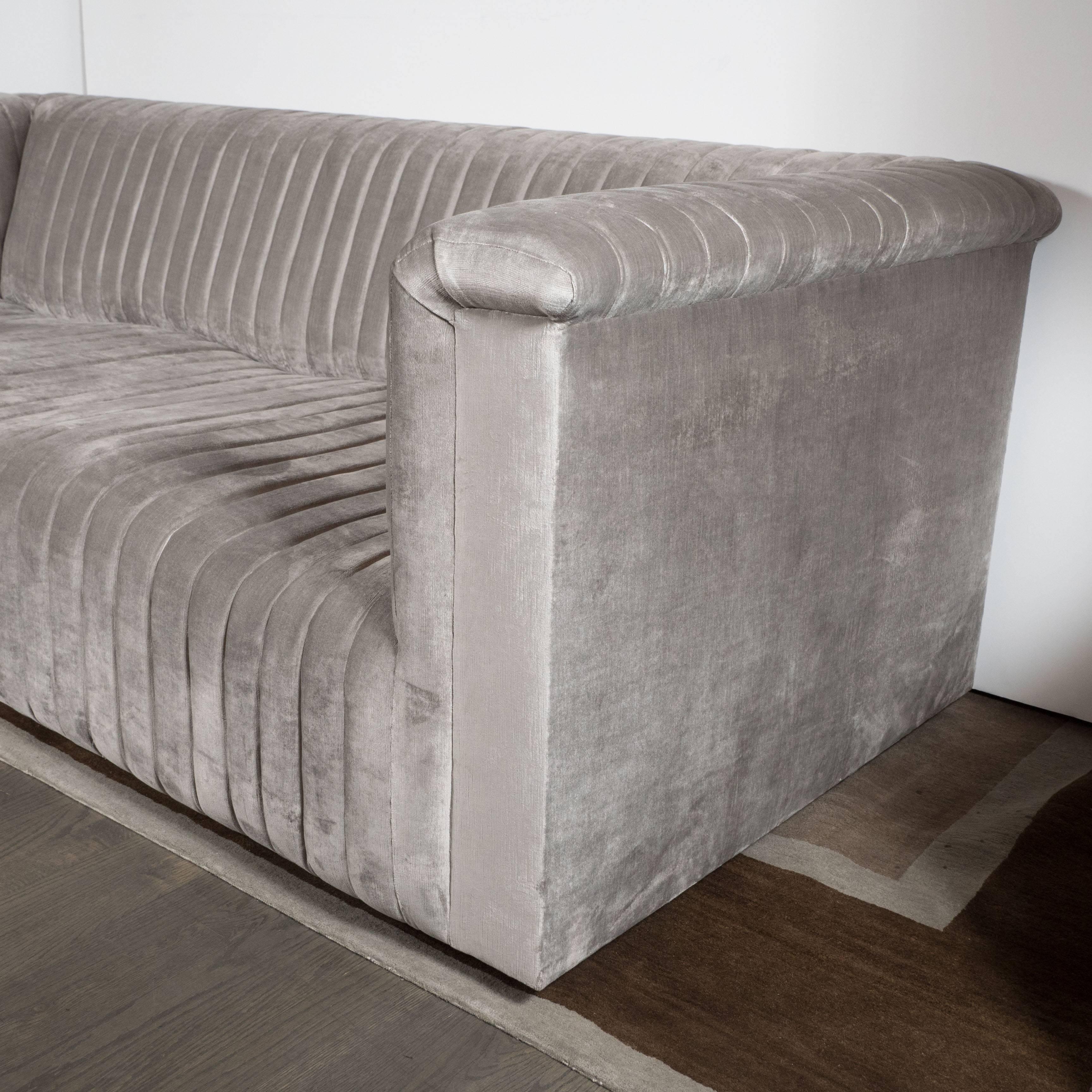A custom modernist channel design sofa in platinum velvet upholstery. Vertical bands form a wave-like pattern across the seat. The channel design continues along the arms and seat back of the sofa. It has been fully upholstered in a luxe platinum