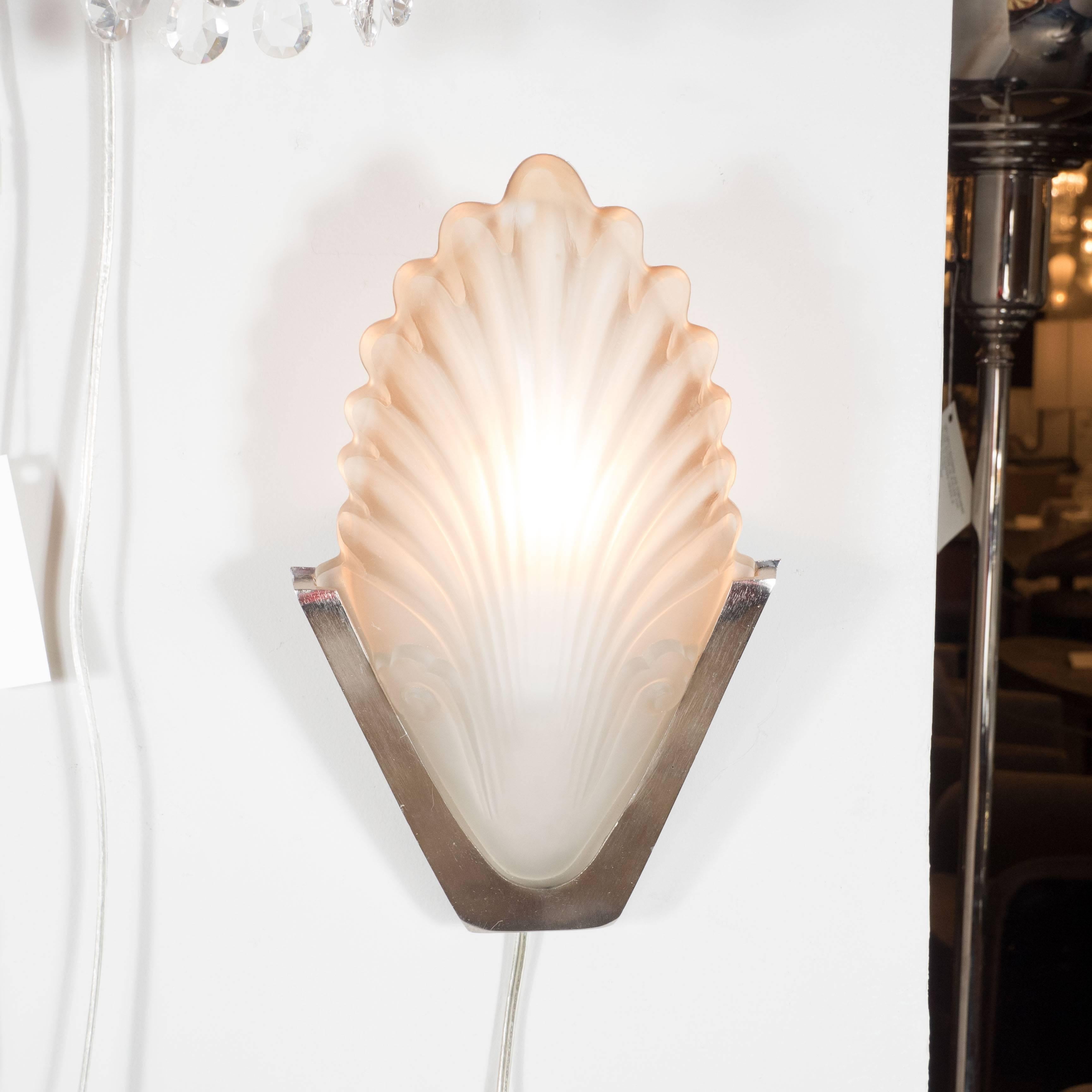 A French Art Deco frosted glass shell sconce with nickeled bronze fittings. A V-shaped backplate supports a single, frosted textured glass shade with ombre smoked amber accents resembling a shell with plume-like detailing. This sconce is fitted with