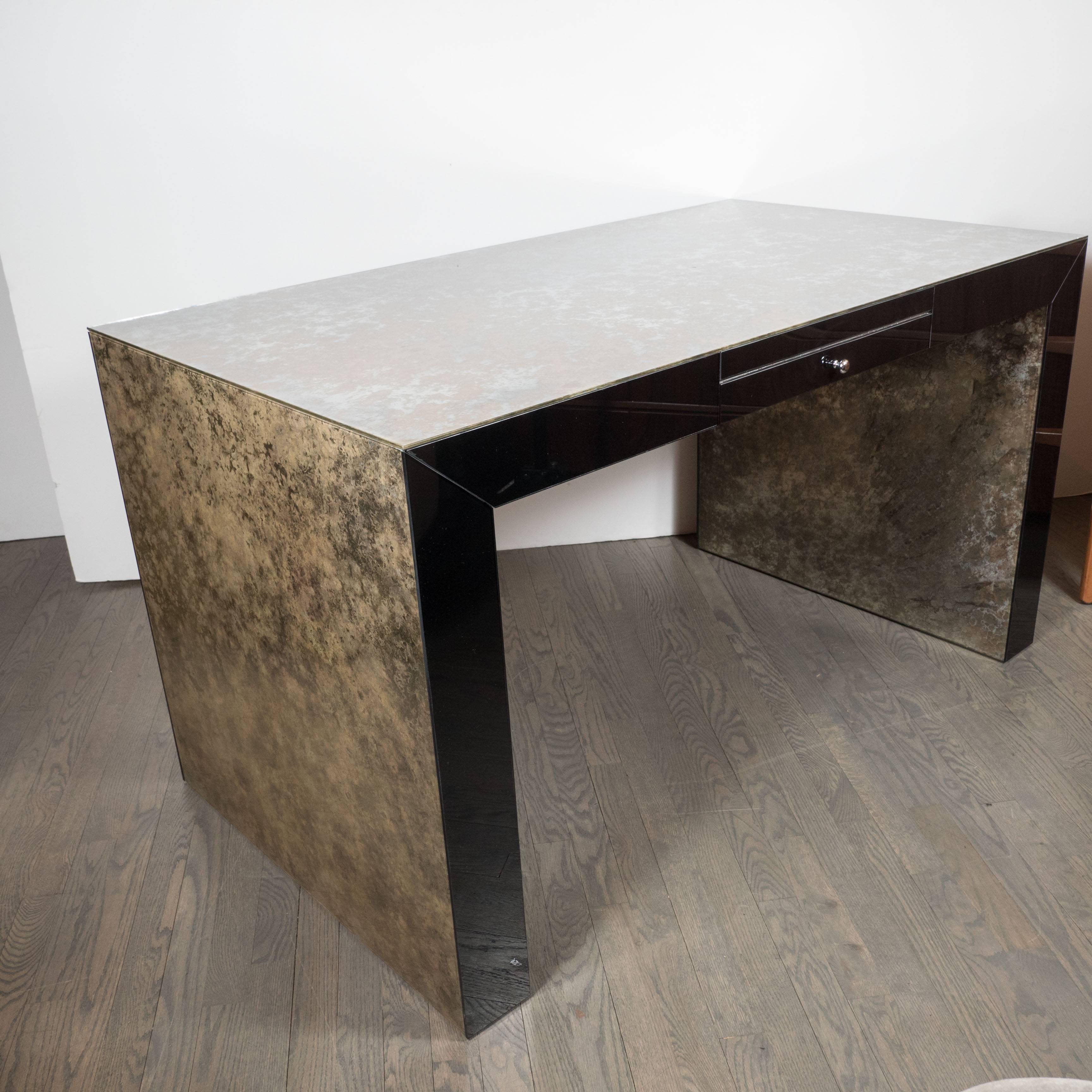 This very clean and modernist Parsons style desk is made of gorgeous antique mirror with borders of black vitrolite. The top and sides of this piece feature a stunning highly spotted and smokey antique mirror while the front and back of the desk are