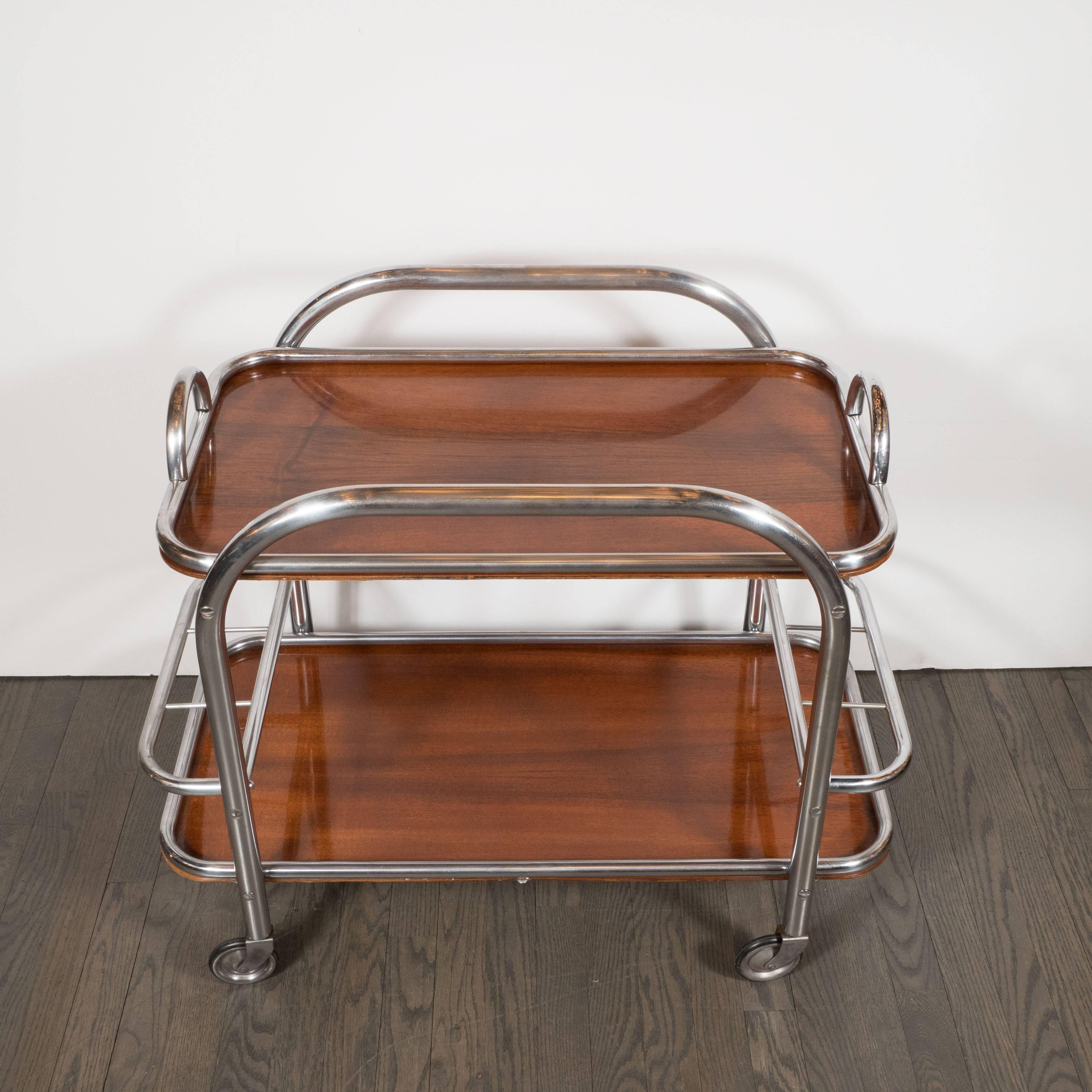 This Art Deco bar cart is made of tubular chrome with inset book-matched walnut two tiers. The top tier is a removable tray that would be wonderful for serving. The bottom tray is affixed to the bar cart. A great example of the Machine Age influence