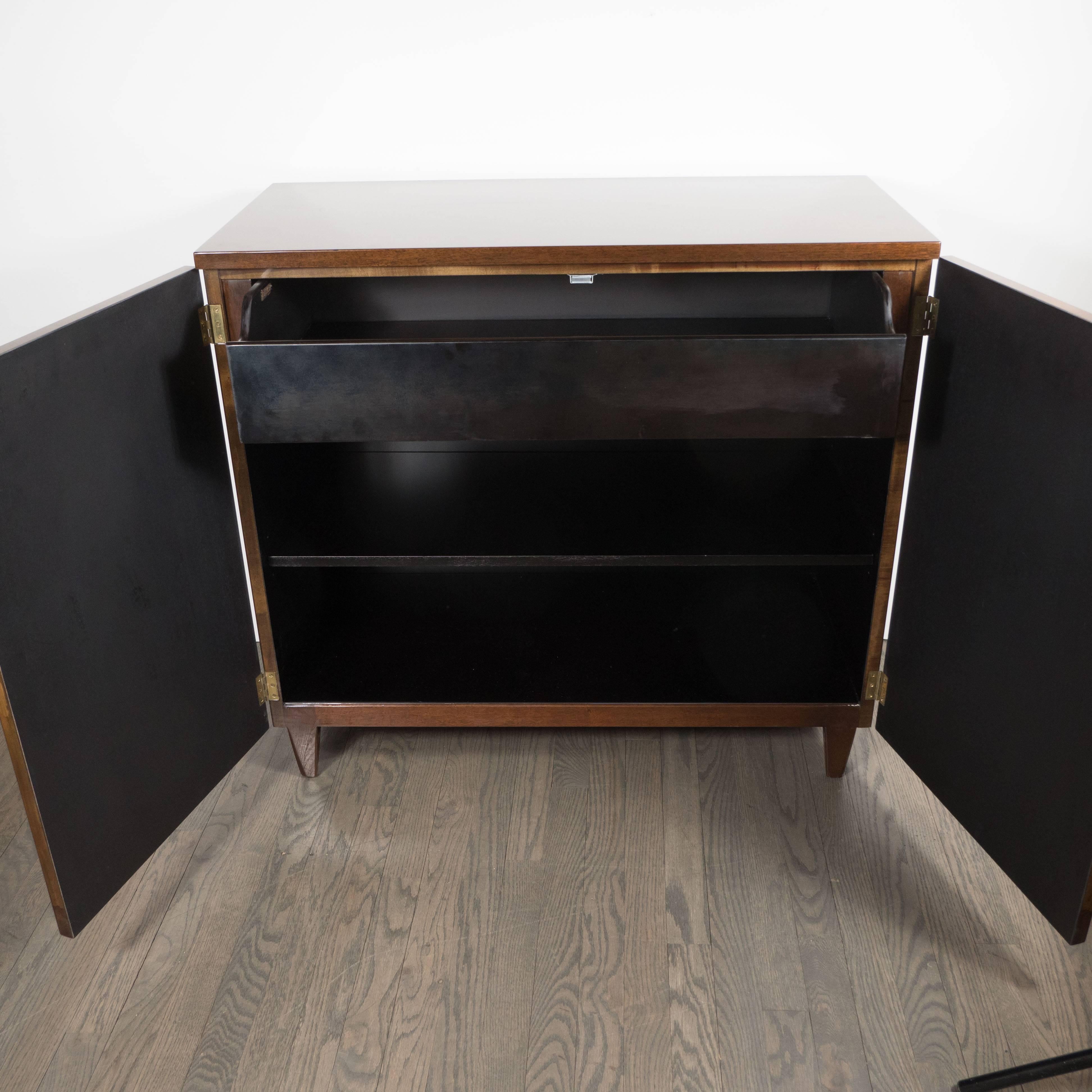 This beautiful pair of Walnut Cabinets features book-matched walnut facades, tapered conical legs and brass hinges. The interior of the dressers, with spacious slide-out drawers and two shelves, is fabricated from ebonized walnut. The wood grain of