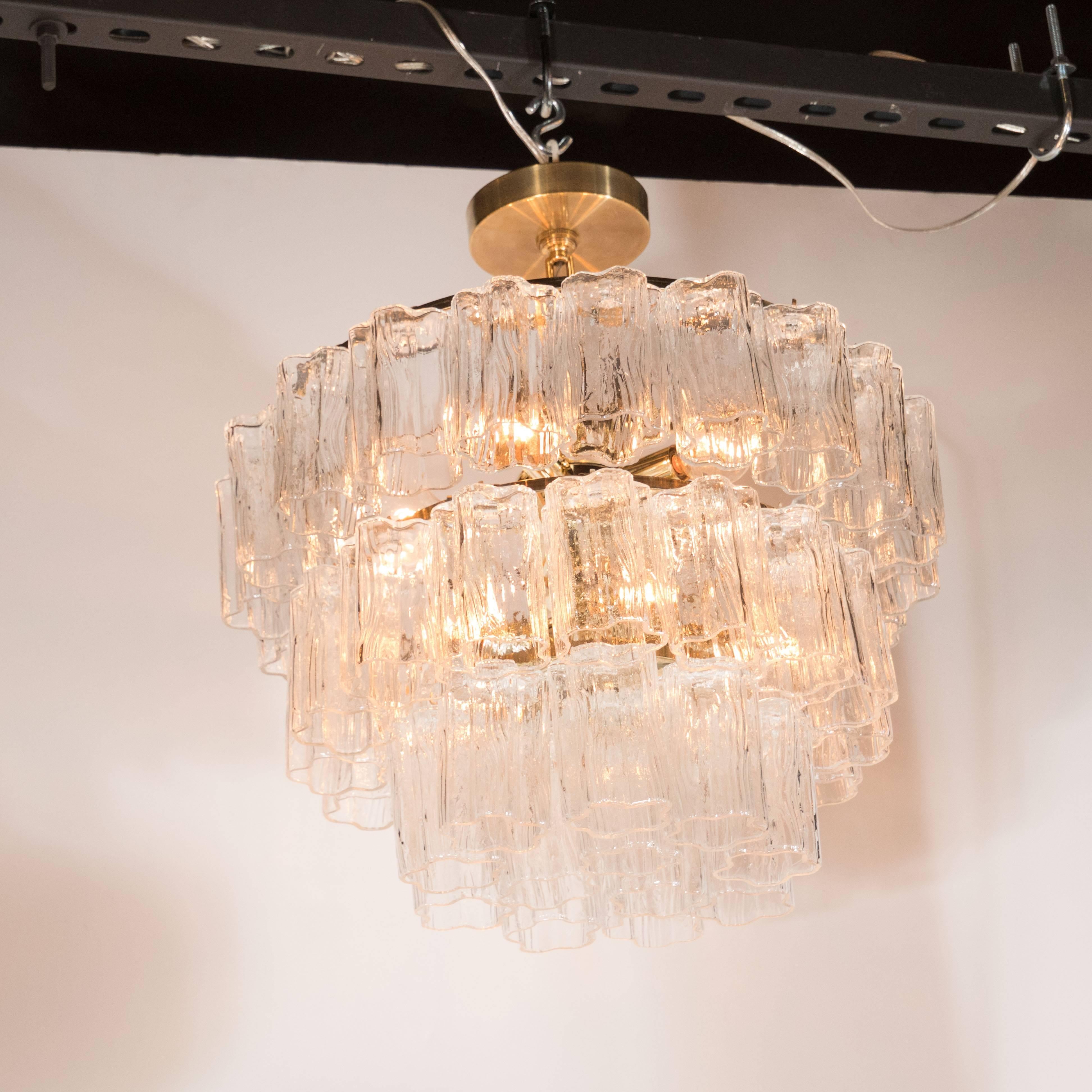 A Mid-Century Modernist three-tier Murano glass tronchi chandelier with brass fittings. Three tiers of cascading, independently hung tronchi pieces surround a polished brass frame. This fixture is fitted with six standard candelabra-style sockets,