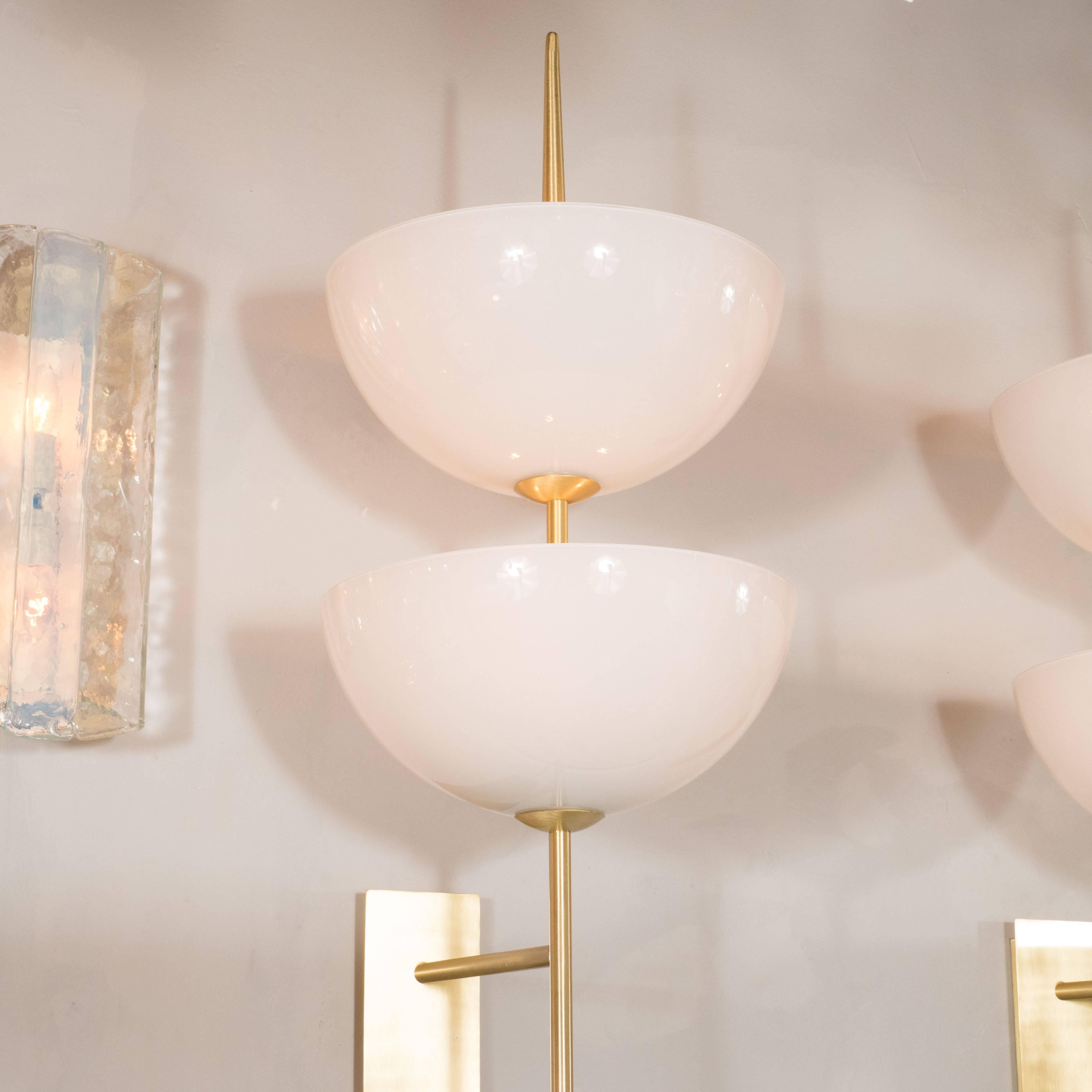 A pair of reverse-dome trophy sconces in milk glass and polished brass. Rectangular back plates support a brass spear-shaped arm with two floating reverse-dome milk glass shades, each housing a pair of up to 60W Edison-based sockets, totaling four