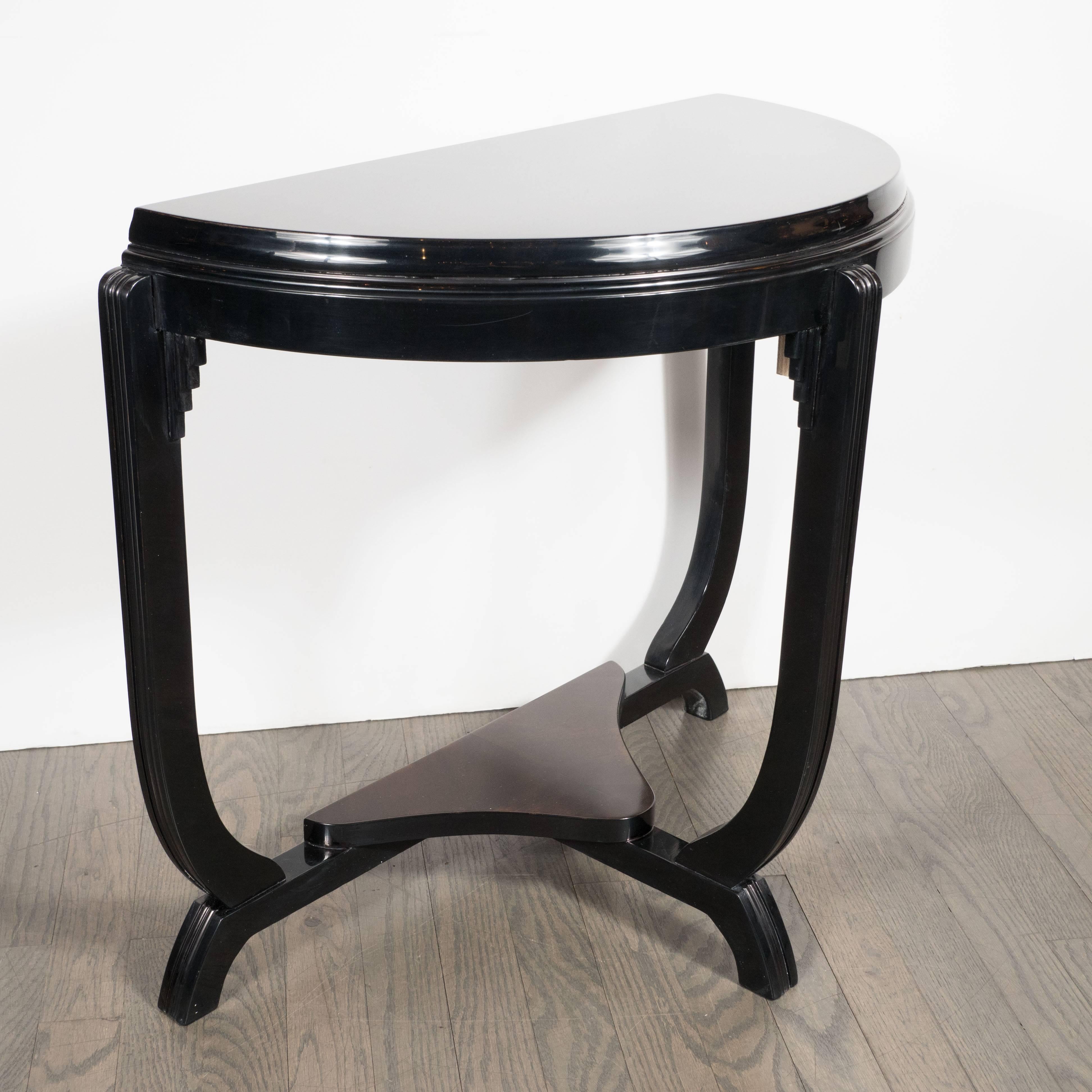 This streamline demilune table, composed of book-matched burled walnut and mahogany, features stunning details including the skyscraper style embellishments at the joints, finely striated buttresses, and ebonized details. The top features an inlaid