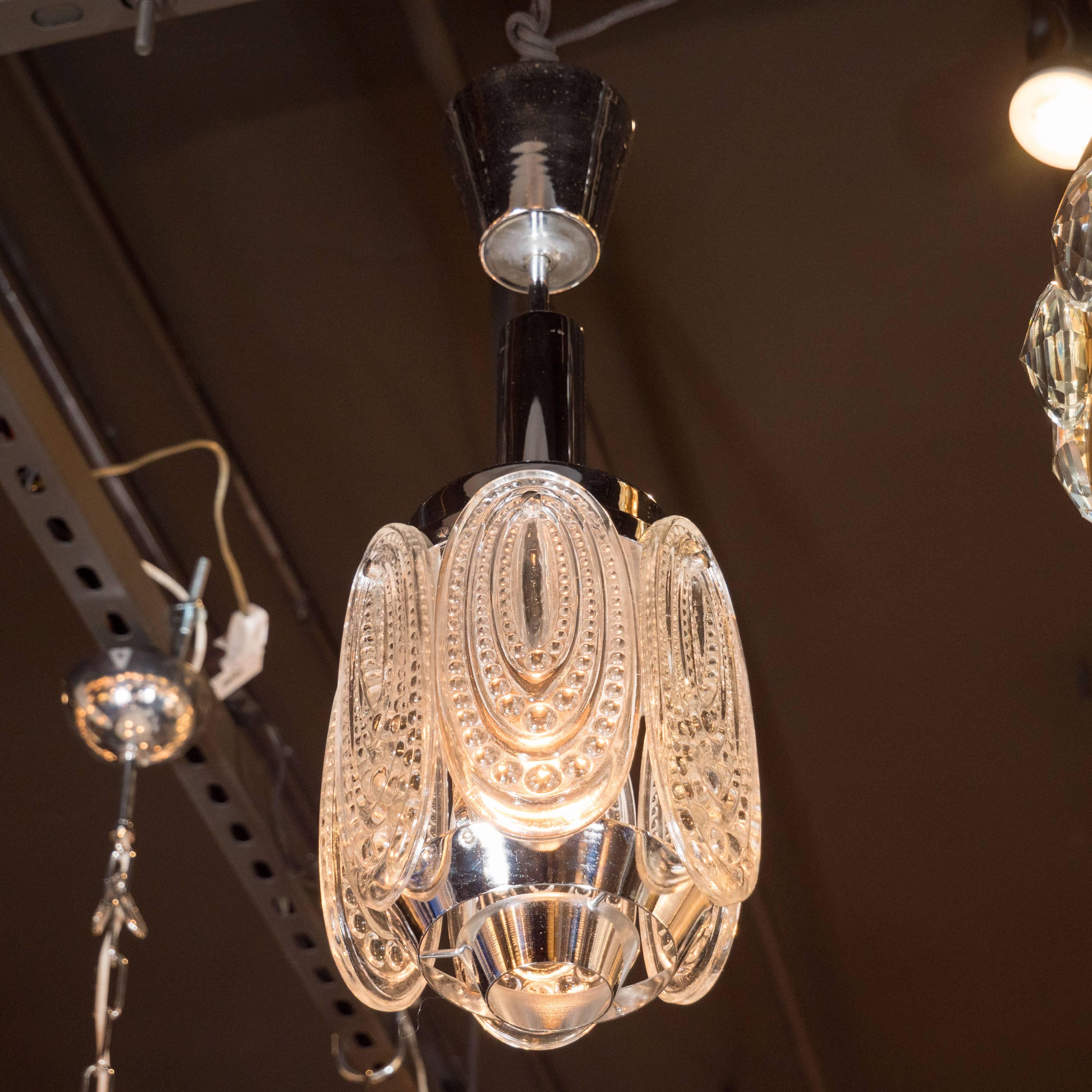 This Mid-Century Modernist pendant features an ornate concentric oval pattern in beaded relief inscribed on each of the six glass petals and polished nickel fittings. This clean and sophisticated design would match well with virtually any style of