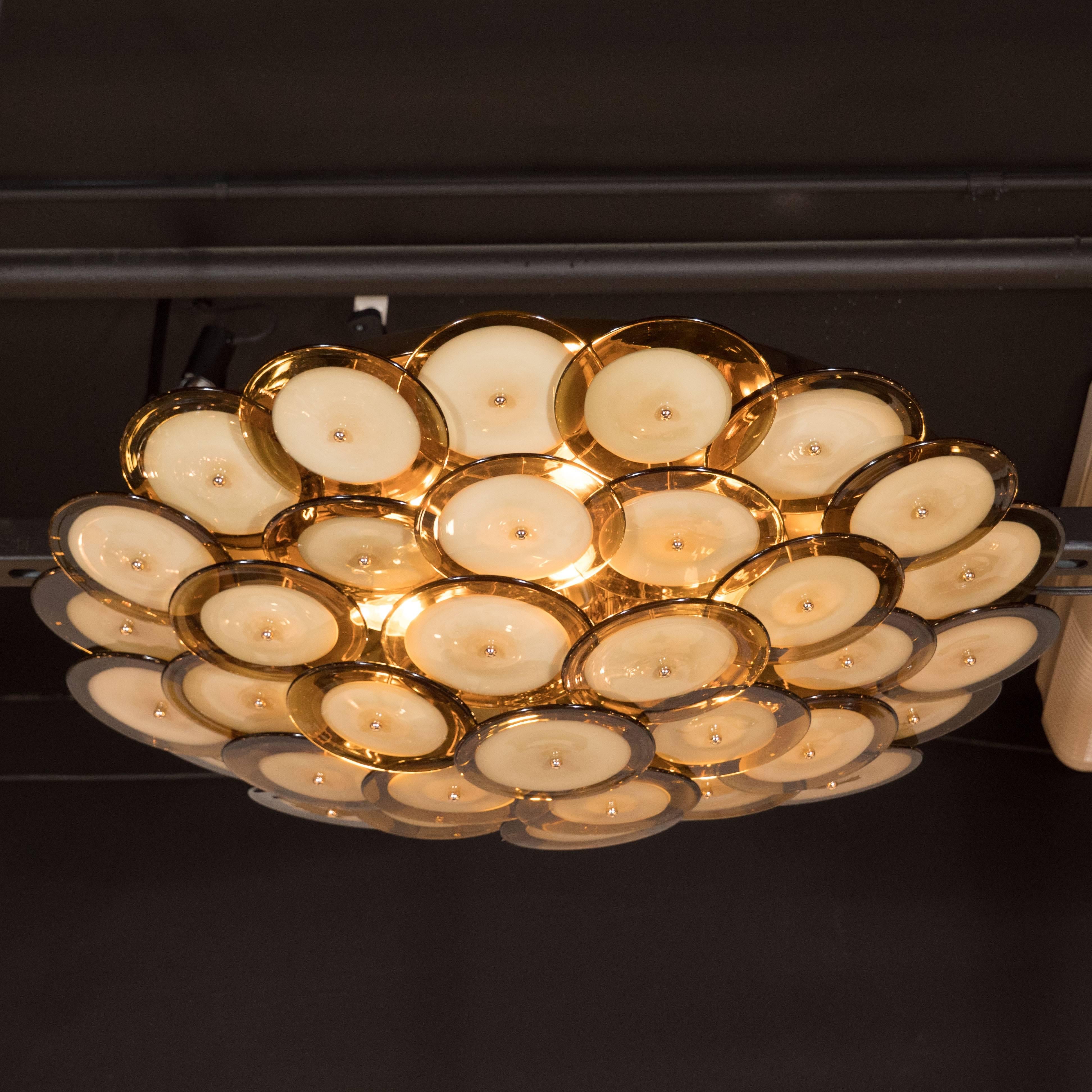This handblown Murano chandelier is composed of an abundance of overlapping disks with smoked topaz perimeters and opaque oyster shell centres attached to a polished brass base. The disks are connected to the base by brass rods, whose ends gently