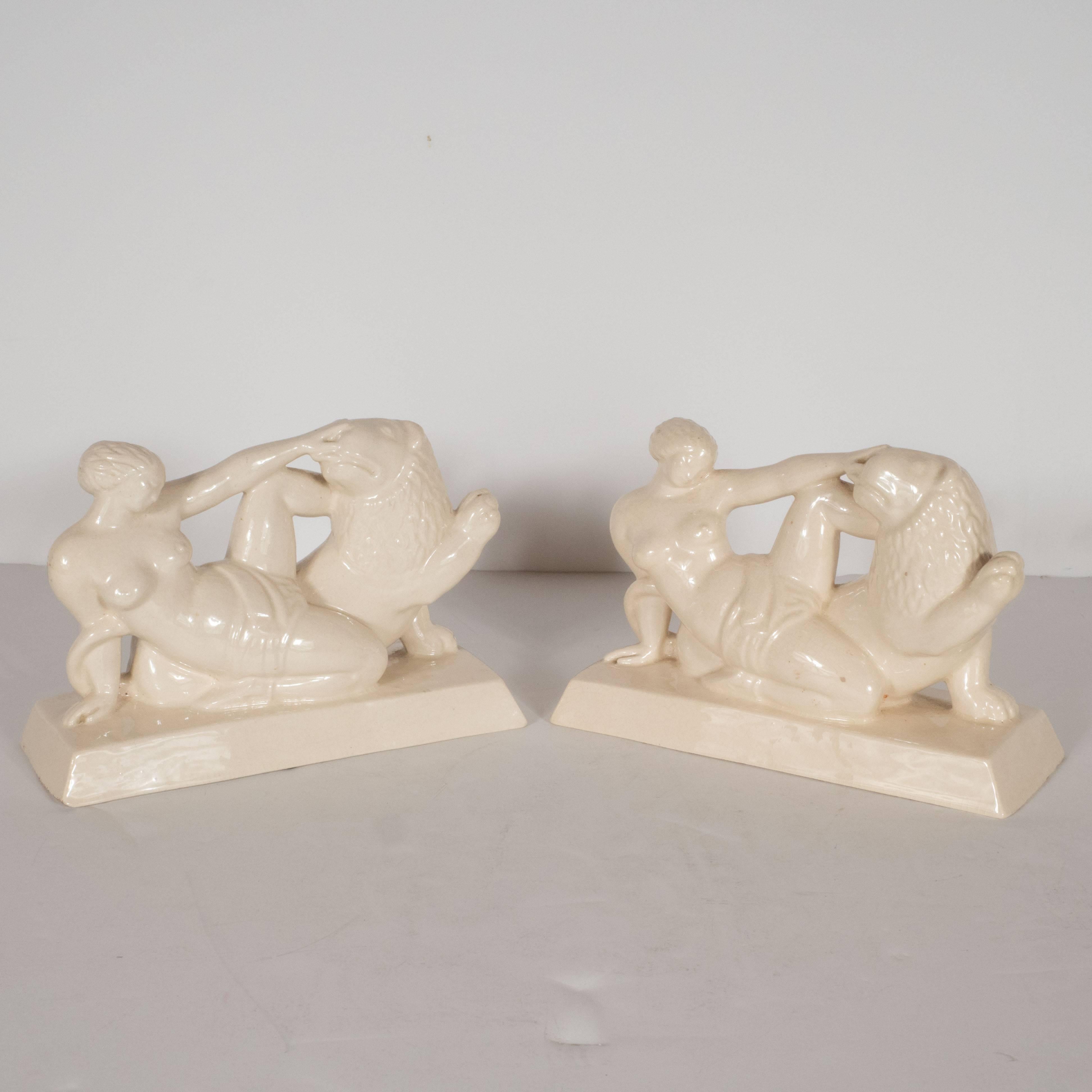 This lovely pair of bookmarks, depicting a nude female figure petting the head of a lion, is rendered in a style suggestive of a Classical Greek tableau. It has been realized in white glazed ceramic which features a very subtle craquelure finish.