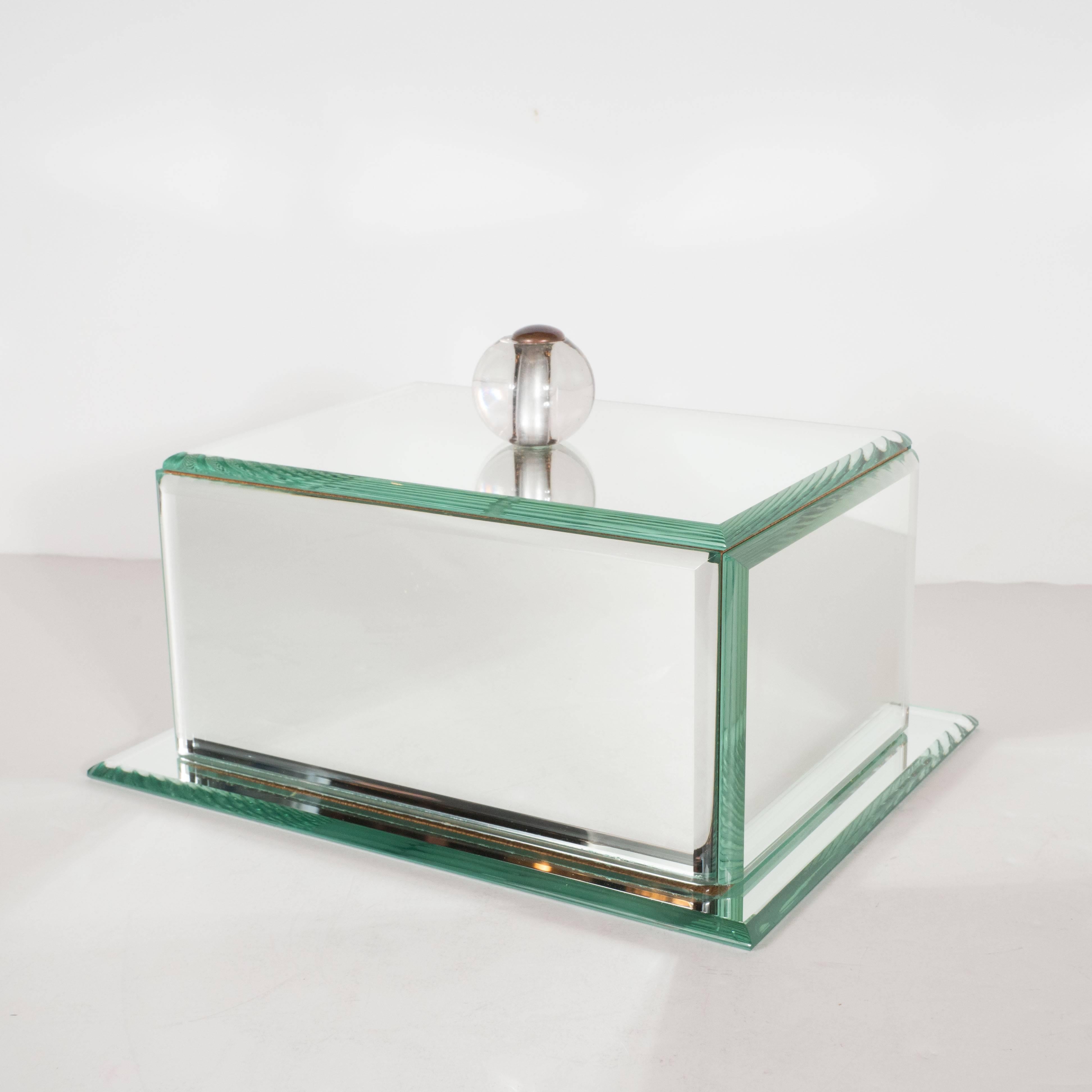 This refined Art Deco mirrored glass box features round beveled edges and a glass ball pull attached with a patined bronze rivet. The object includes a mirrored base that extends slightly beyond the perimeter of the box. The inside of the box has
