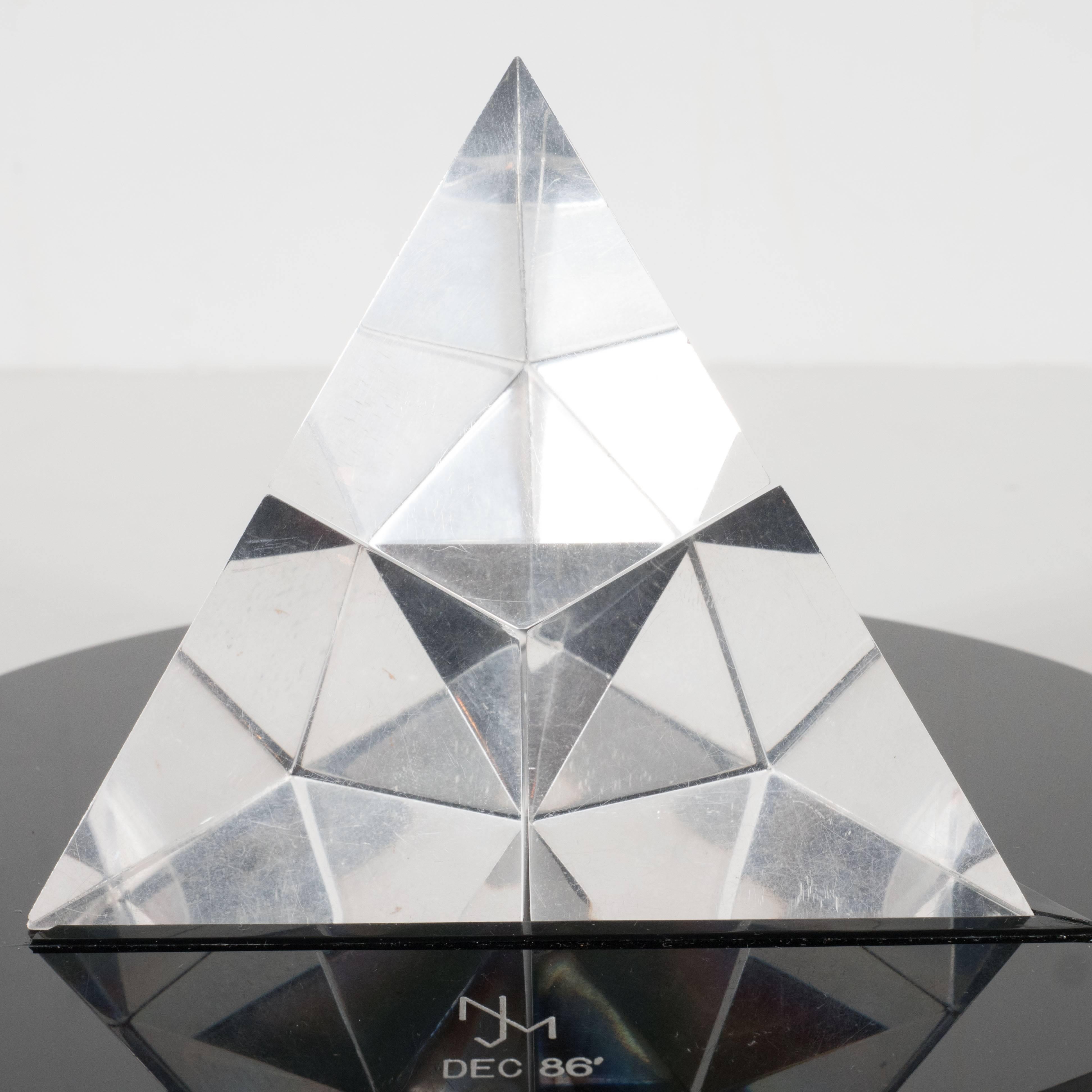This dynamic Modernist pyramid sculpture is composed of four beveled pieces of Lucite that fit together like a puzzle. When fully assembled, the structure appears like a radiant pyramid-shaped diamond resting on a circular ebony base. This is truly