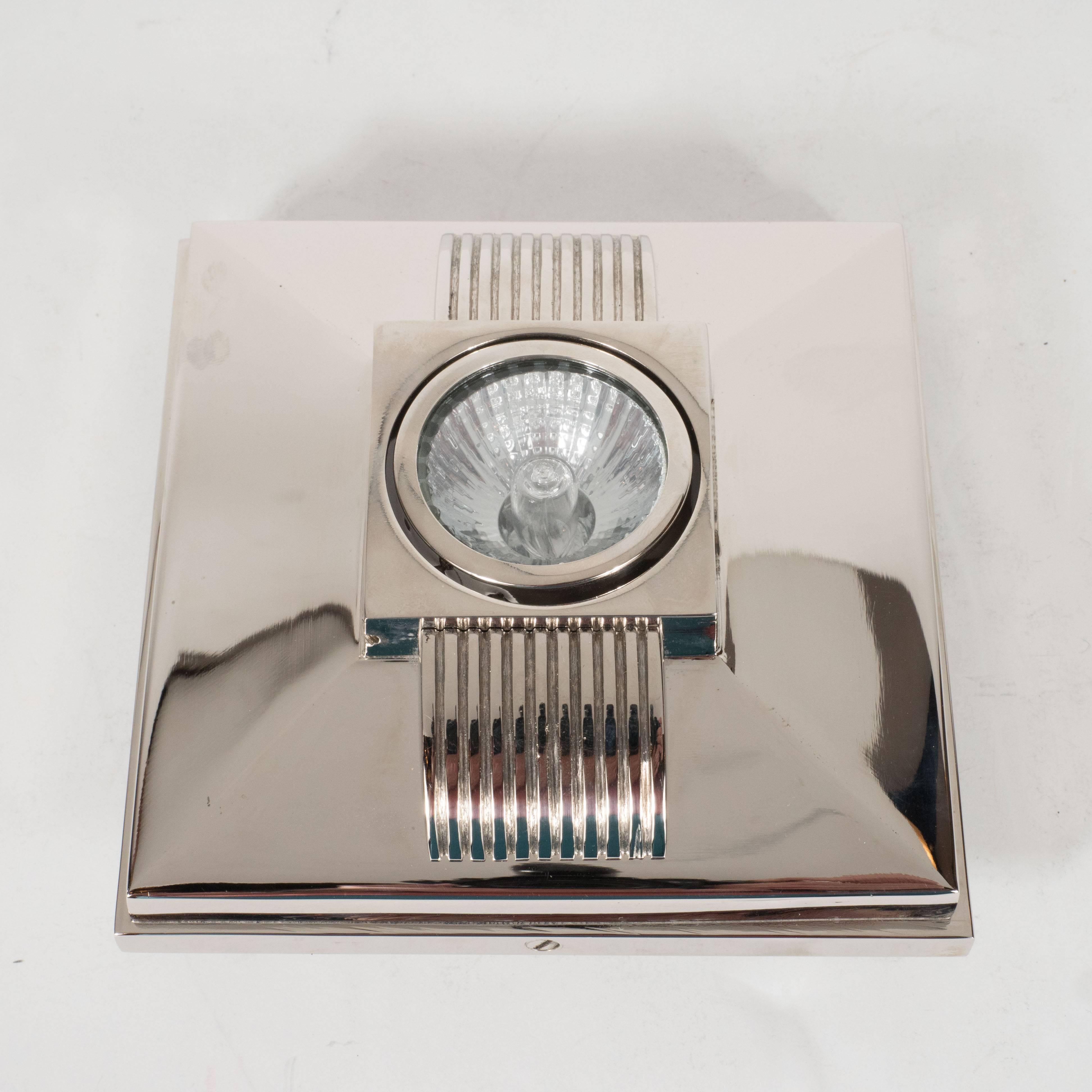 This stunning skyscraper style spotlight, in polished nickel, features sloping sides with ribbed detailing. In the center of the fixture lies a square support that holds a single swiveling halogen bulb. This fixture would be perfect for a bathroom,