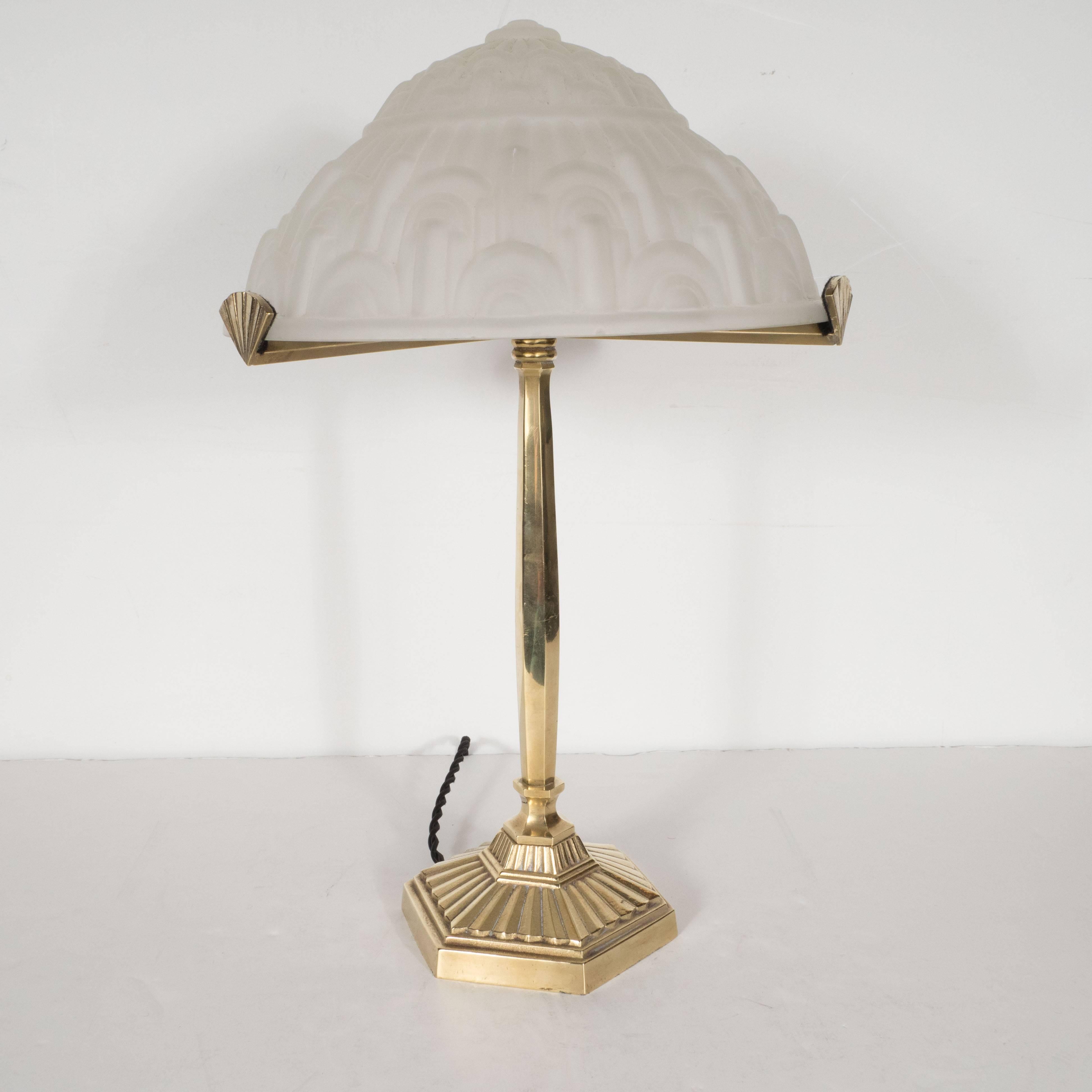 This beautiful Art Deco lamp features a gilded bronze body, three arms with fan embellishments supporting a frosted glass shade with geometric skyscraper style designs. The hexagonal base has been forged in textured gilded bronze and includes a