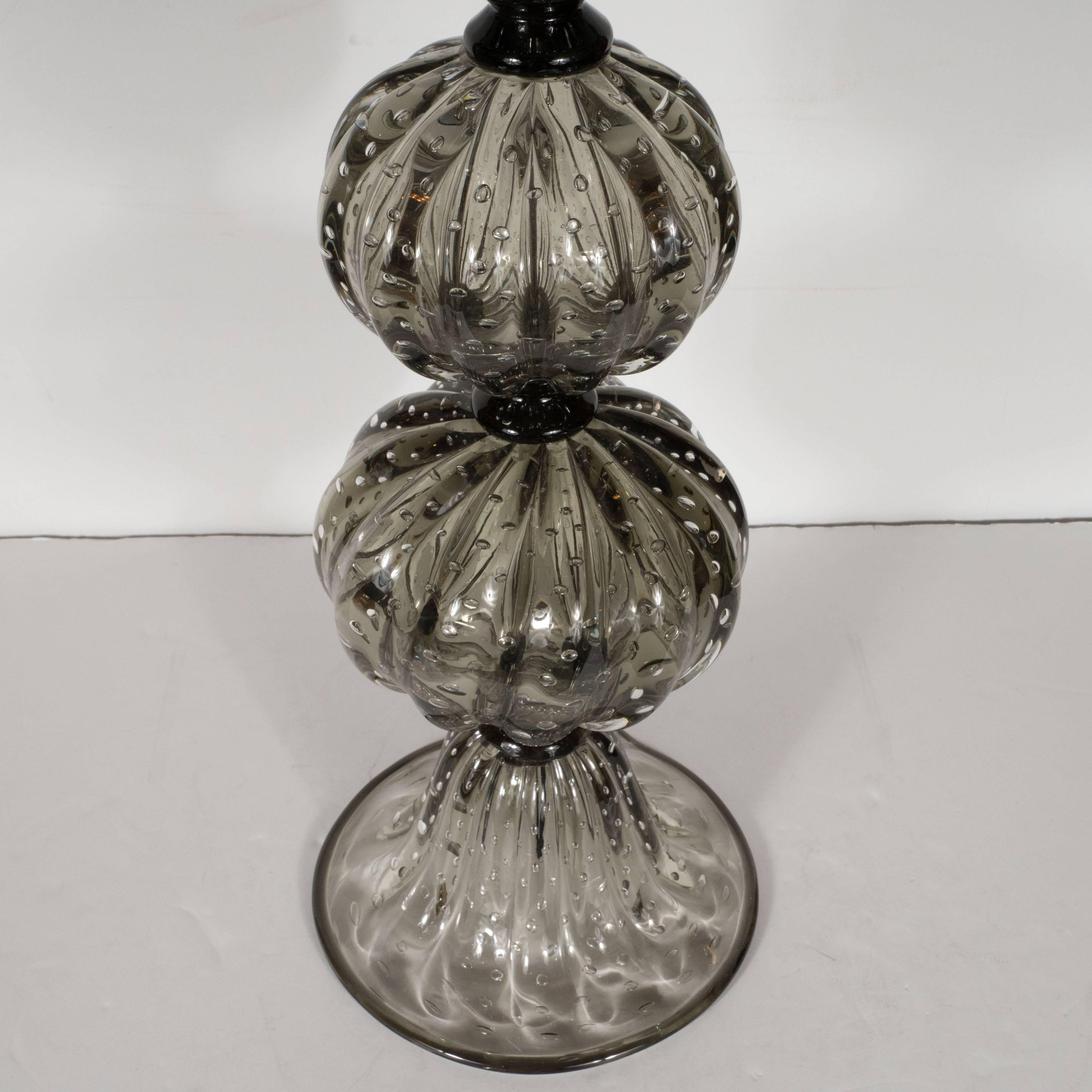 This sophisticated pair of smoked pewter lamps features three orbital forms with raised striations and suspended bubbles and a trumpet shaped base. The billowing forms are cinched in three places by black rings that offer a subtle transparency. The
