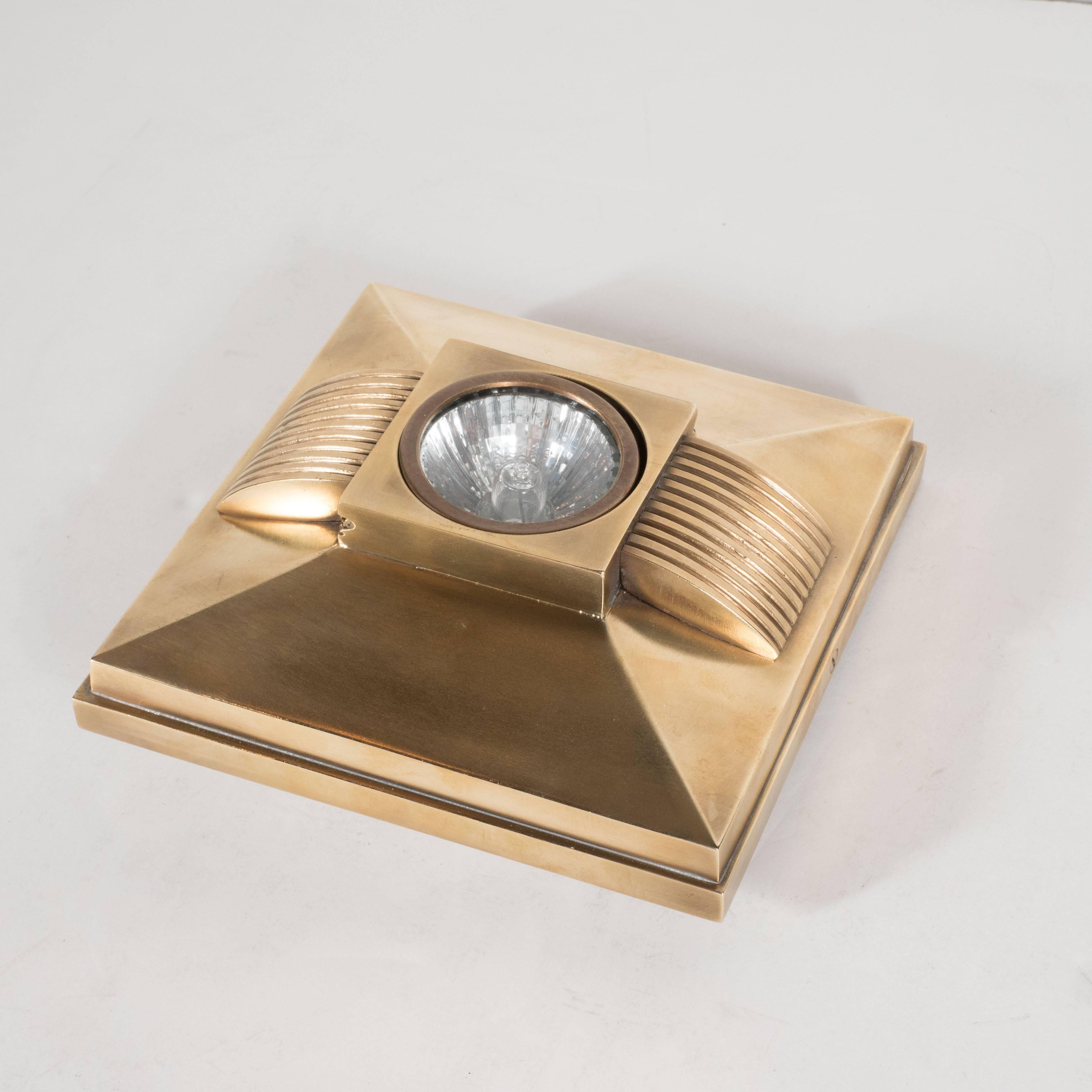 This stunning skyscraper style spotlight, in brushed bronze, features sloping sides with ribbed detailing. In the centre of the fixture lies a square support that holds a single swiveling halogen bulb. This fixture would be perfect for a bathroom,